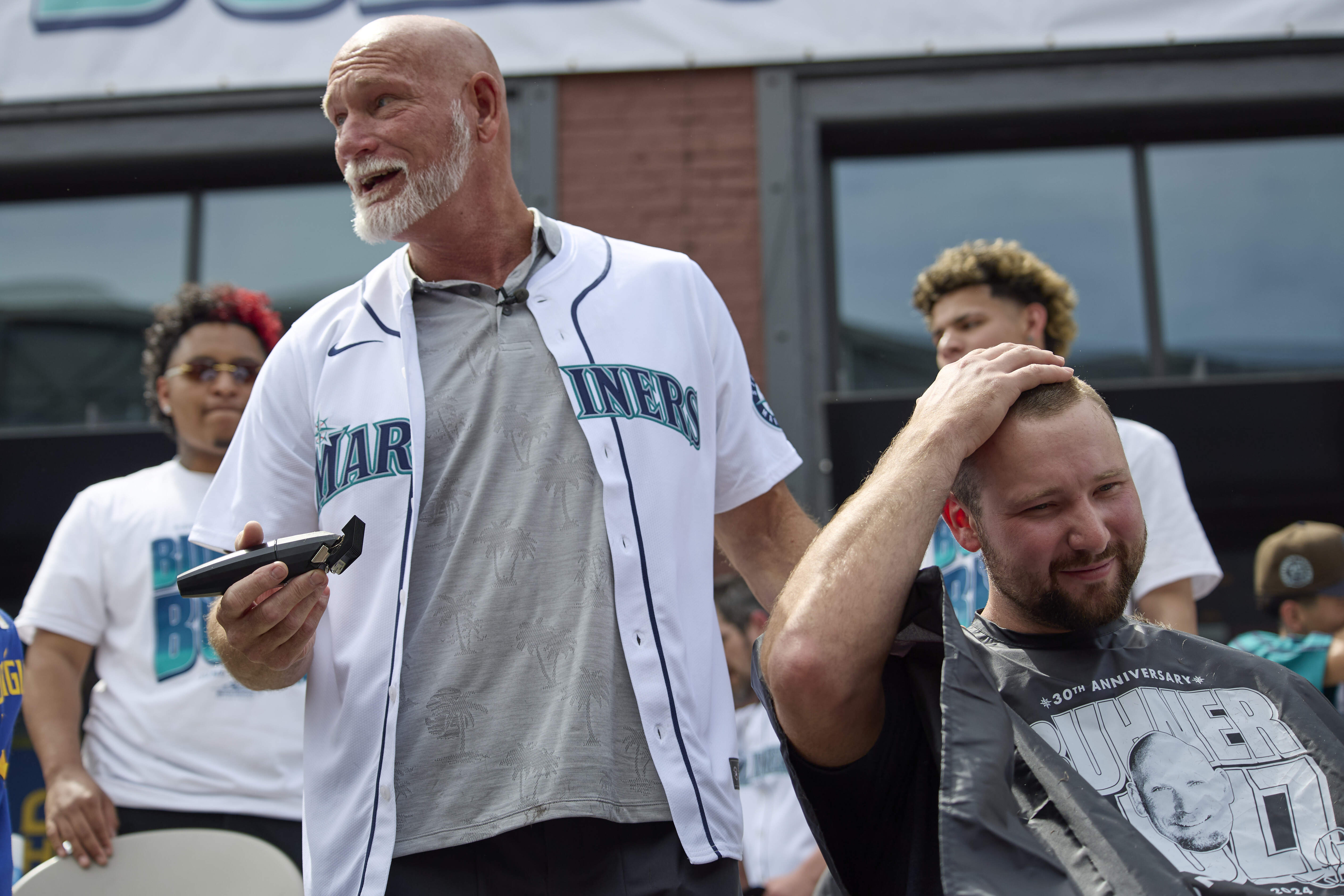 Former Seattle Mariners player Jay Buhner turns and jokes with the crowd as he shaves catcher Cal Raleigh's head on Buhner Buzz Night, Thursday, June 13, 2024, in Seattle. The promotion is based on Buhner's shaved-head style. 