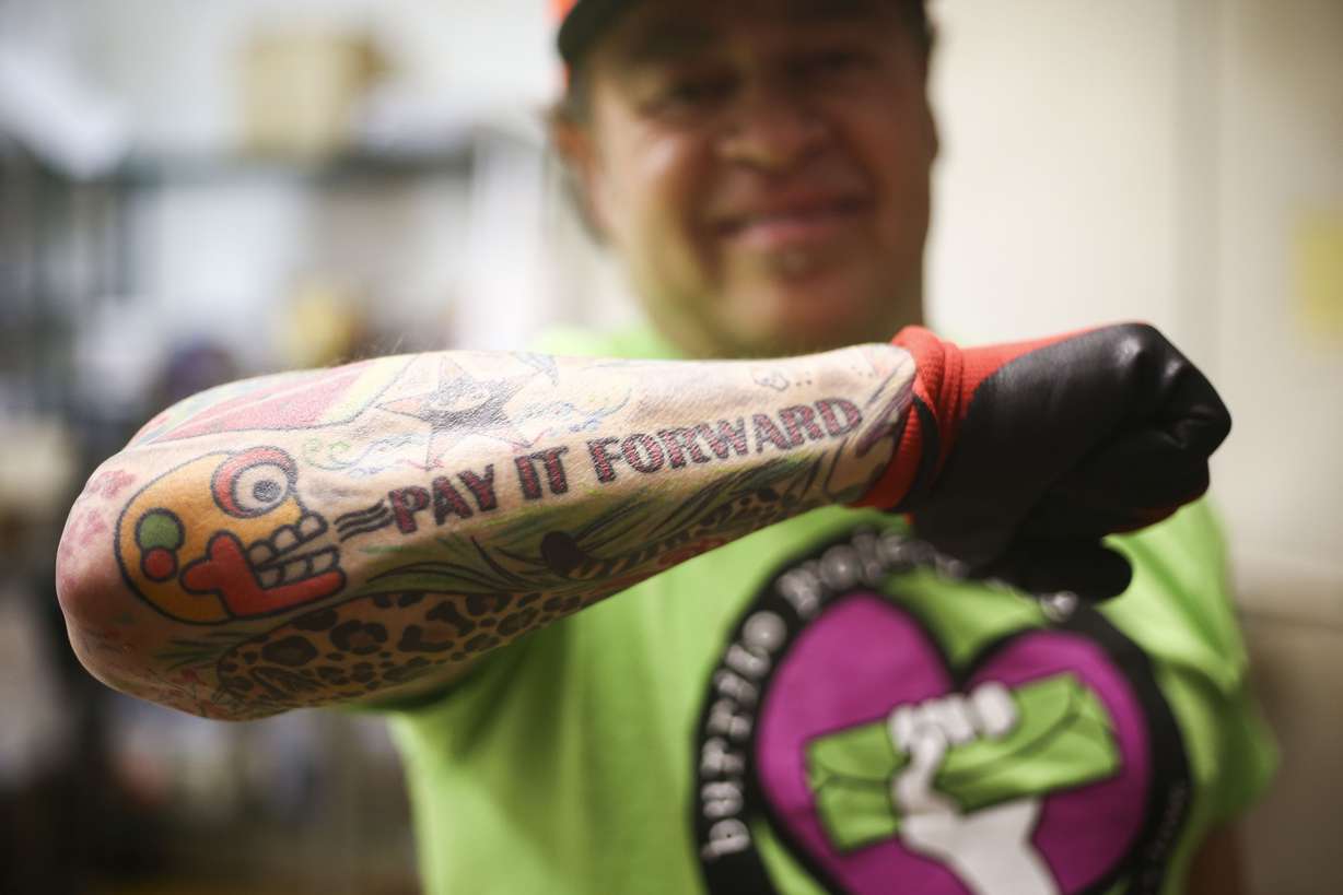 Jorge Fierro, owner of Rico Brand, displays his tattoo reading "pay it forward" the company's headquarters in Salt Lake City, March 7, 2019, while volunteers participate in the Burrito Project.