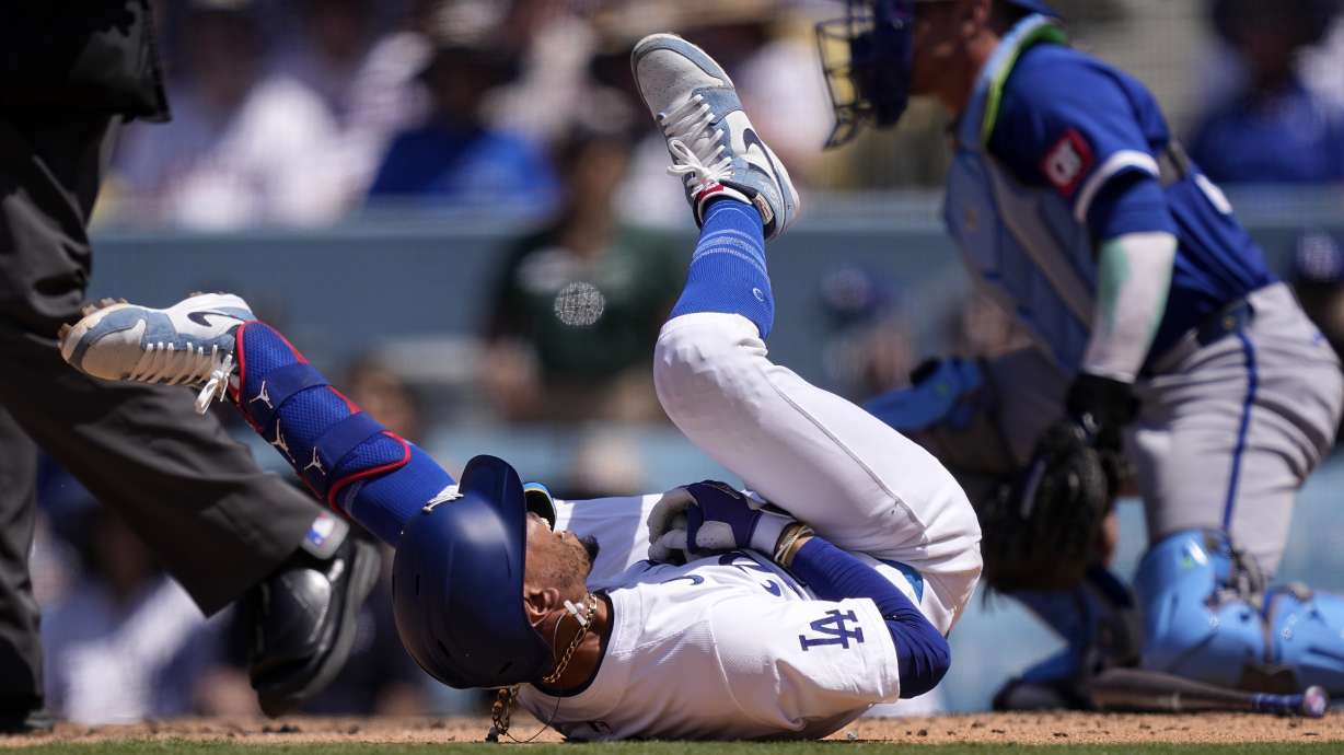 Los Angeles Dodgers' Mookie Betts, left, writhes on the ground after being hit by a pitch as Kansas City Royals catcher Freddy Fermin kneels at the plate during the seventh inning of a baseball game Sunday, June 16, 2024, in Los Angeles.
