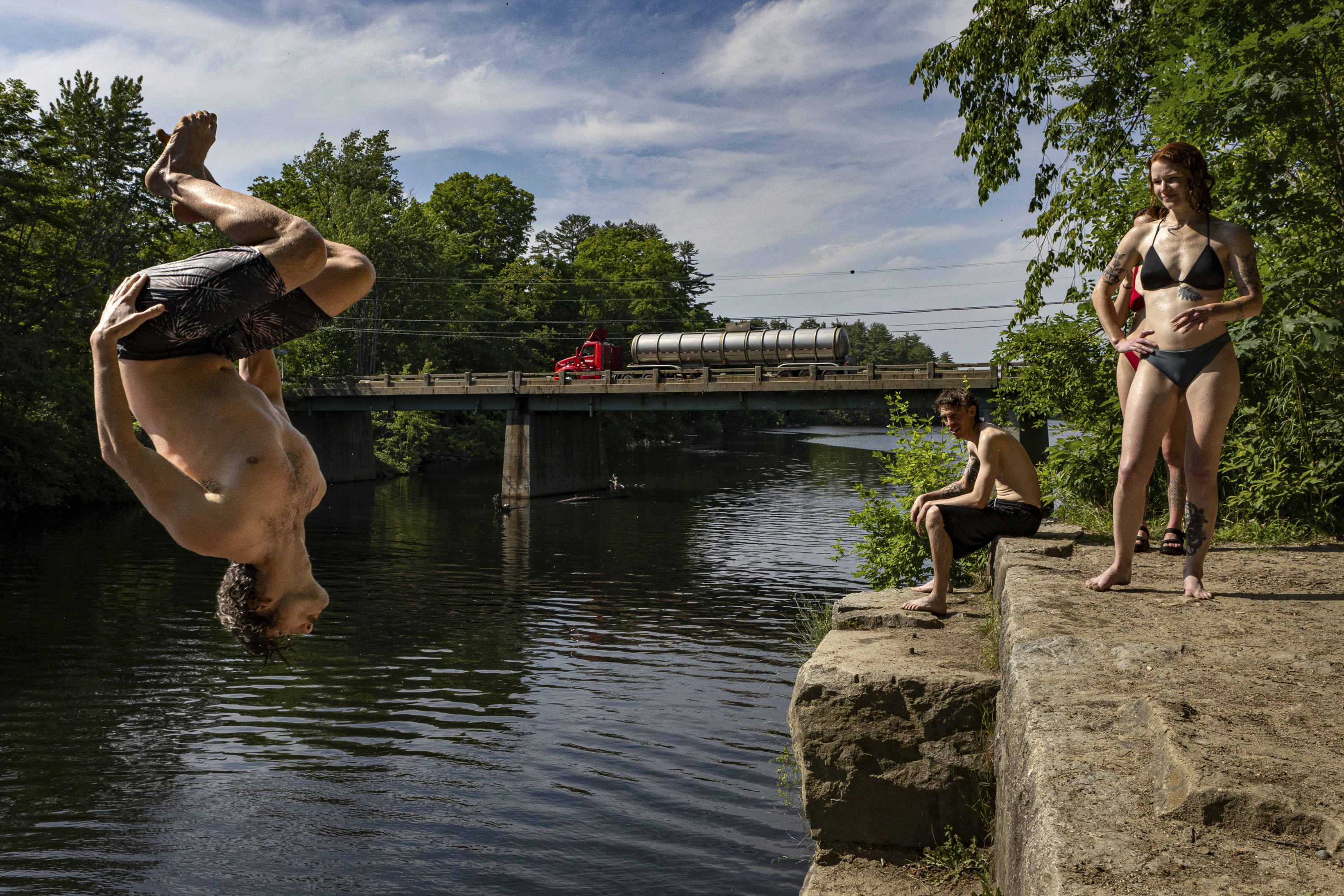 Levi Rush does a backflip off an old bridge abutment into the Saco River in Buxton, Maine, Tuesday. Hot weather is predicted until the end of the week.