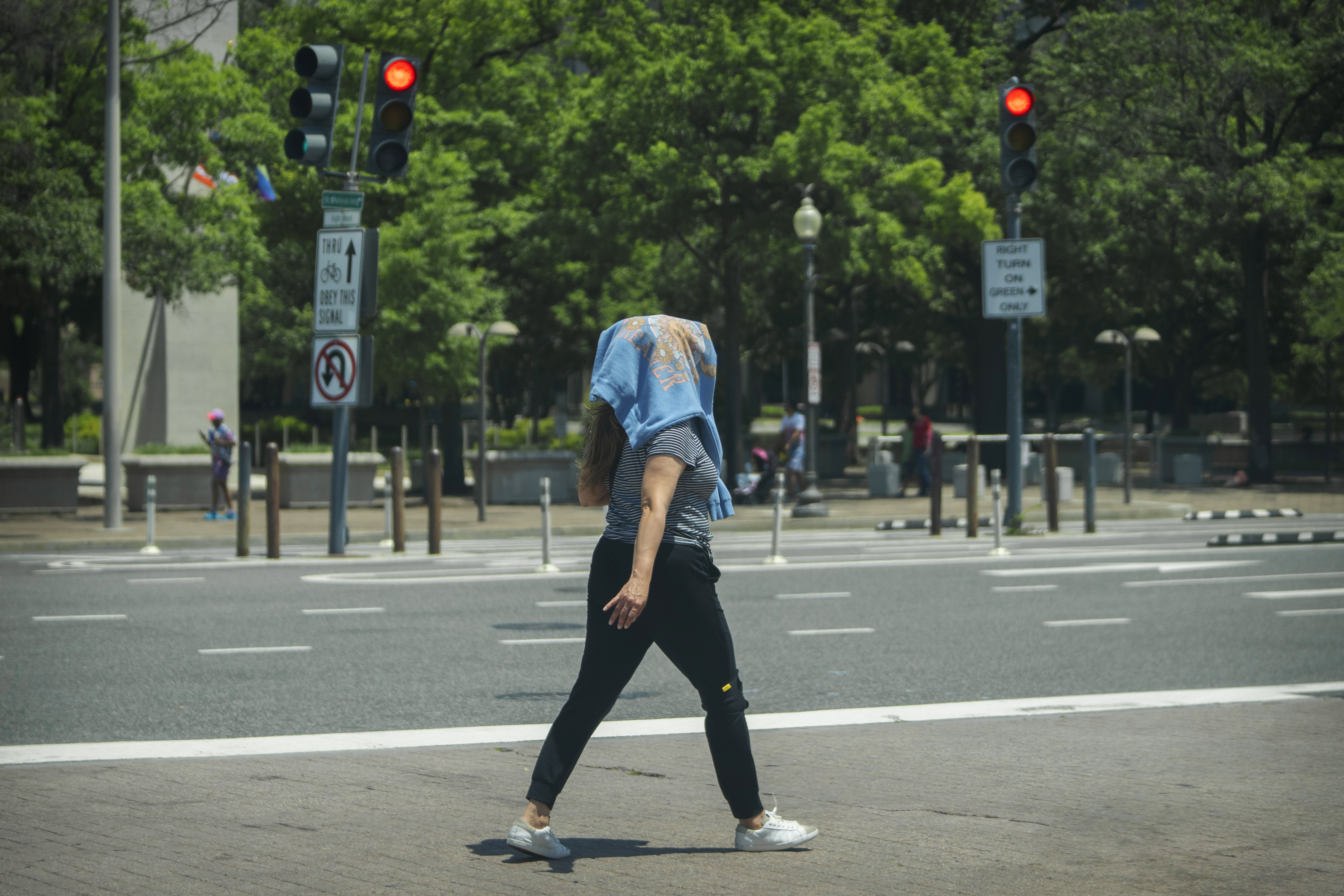 A woman wearing a sweatshirt on her head to protect herself from the sun walks across a crosswalk in downtown Washington, Wednesday. High temperatures are expected to stay in the 90s in the nation's capital for the rest of the week as a heat wave builds into the Northeast.