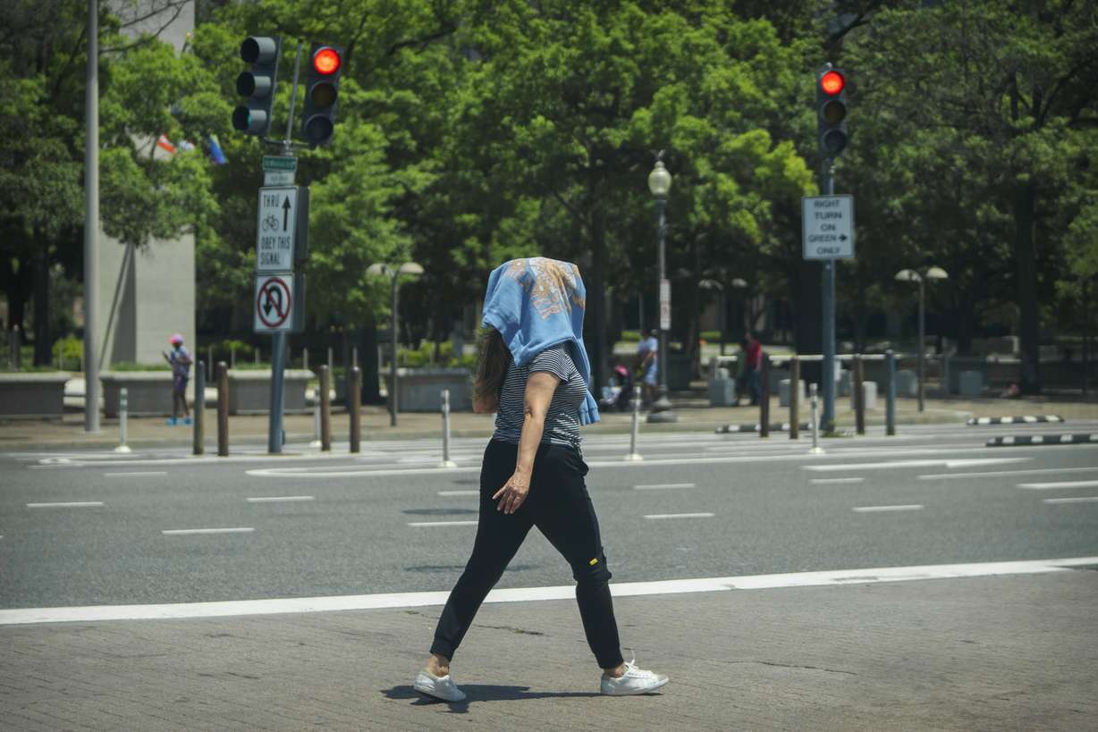 A woman wearing a sweatshirt on her head to protect herself from the sun walks across a crosswalk in downtown Washington, Wednesday. High temperatures are expected to stay in the 90s in the nation's capital for the rest of the week as a heat wave builds into the Northeast.