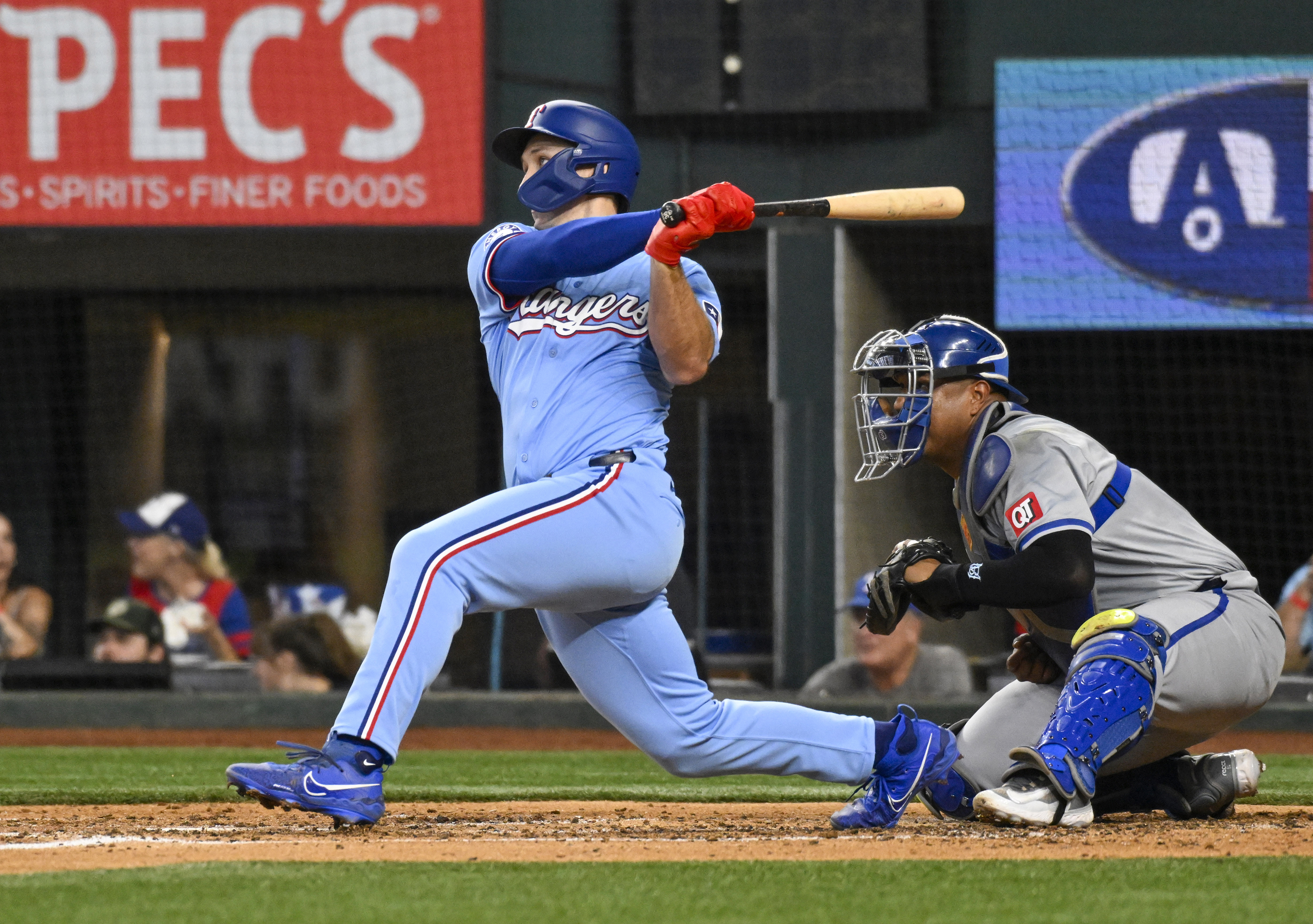 Texas Rangers' Wyatt Langford, left, hits an RBI double in the fifth inning as Kansas City Royals catcher Salvador Perez, right, looks on in a baseball game Sunday, June 23, 2024, in Arlington, Texas.