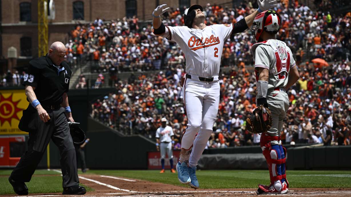 Baltimore Orioles' Gunnar Henderson (2) celebrates his home run in front of Philadelphia Phillies catcher Garrett Stubbs, right, during the first inning of a baseball game, Sunday, June 16, 2024, in Baltimore. Home plate umpire Mike Estabrook looks on at left.