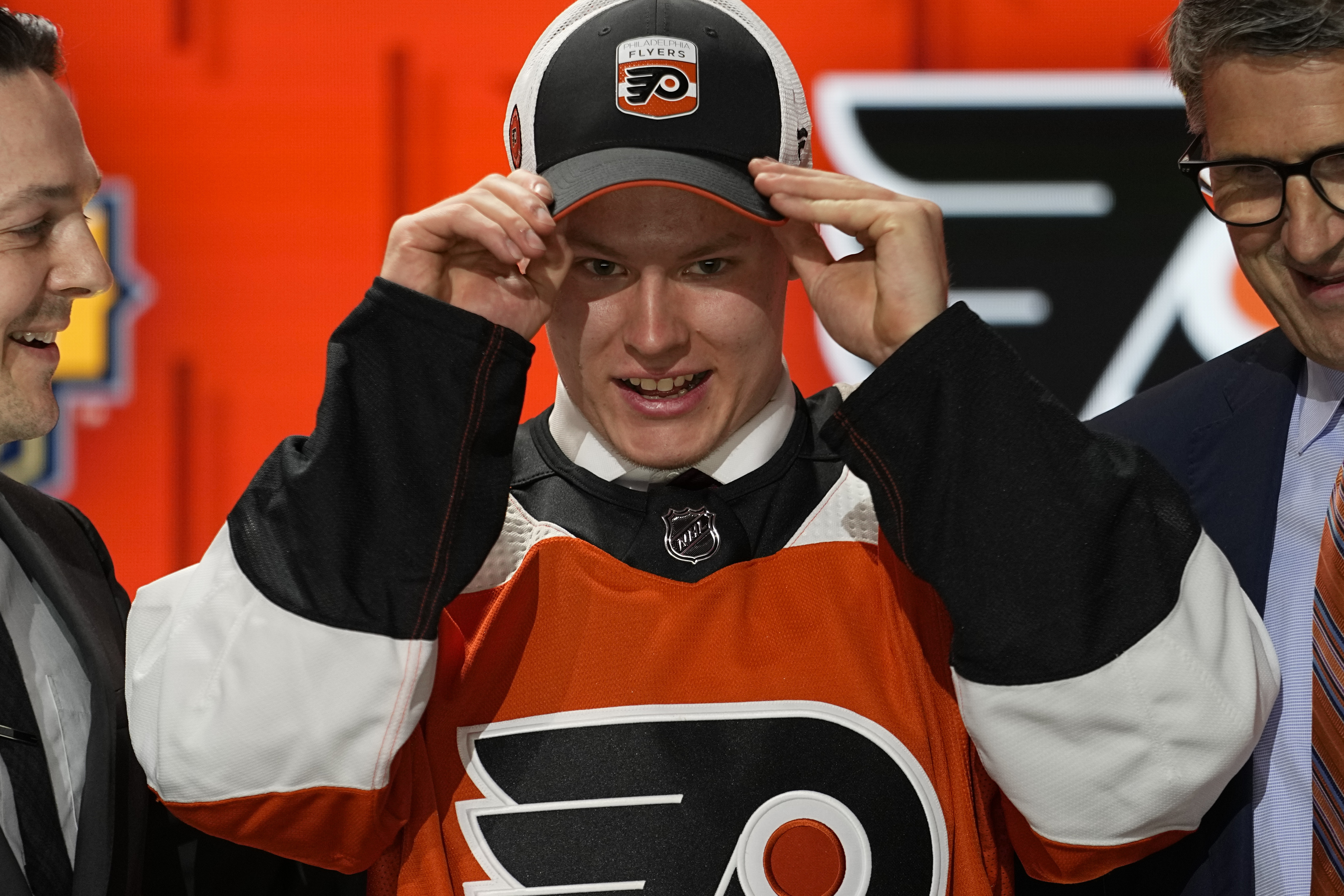FILE - Matvei Michkov, center, adjusts his Philadelphia Flyers cap after being picked by the team during the first round of the NHL hockey draft June 28, 2023, in Nashville, Tenn. A person with knowledge of the situation tells The Associated Press that top Flyers prospect Michkov is being released by KHL club SKA Saint Petersburg. The move is the first step toward Michkov joining the Flyers ahead of the schedule.