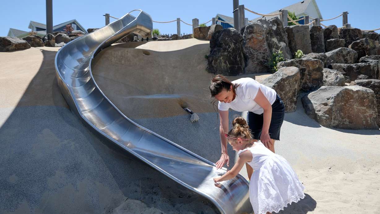 Meredith Sherwood and her daughter June Sherwood, 3, test the temperature of a slide on a hot summer day at Brookeside Park in South Jordan on Tuesday.