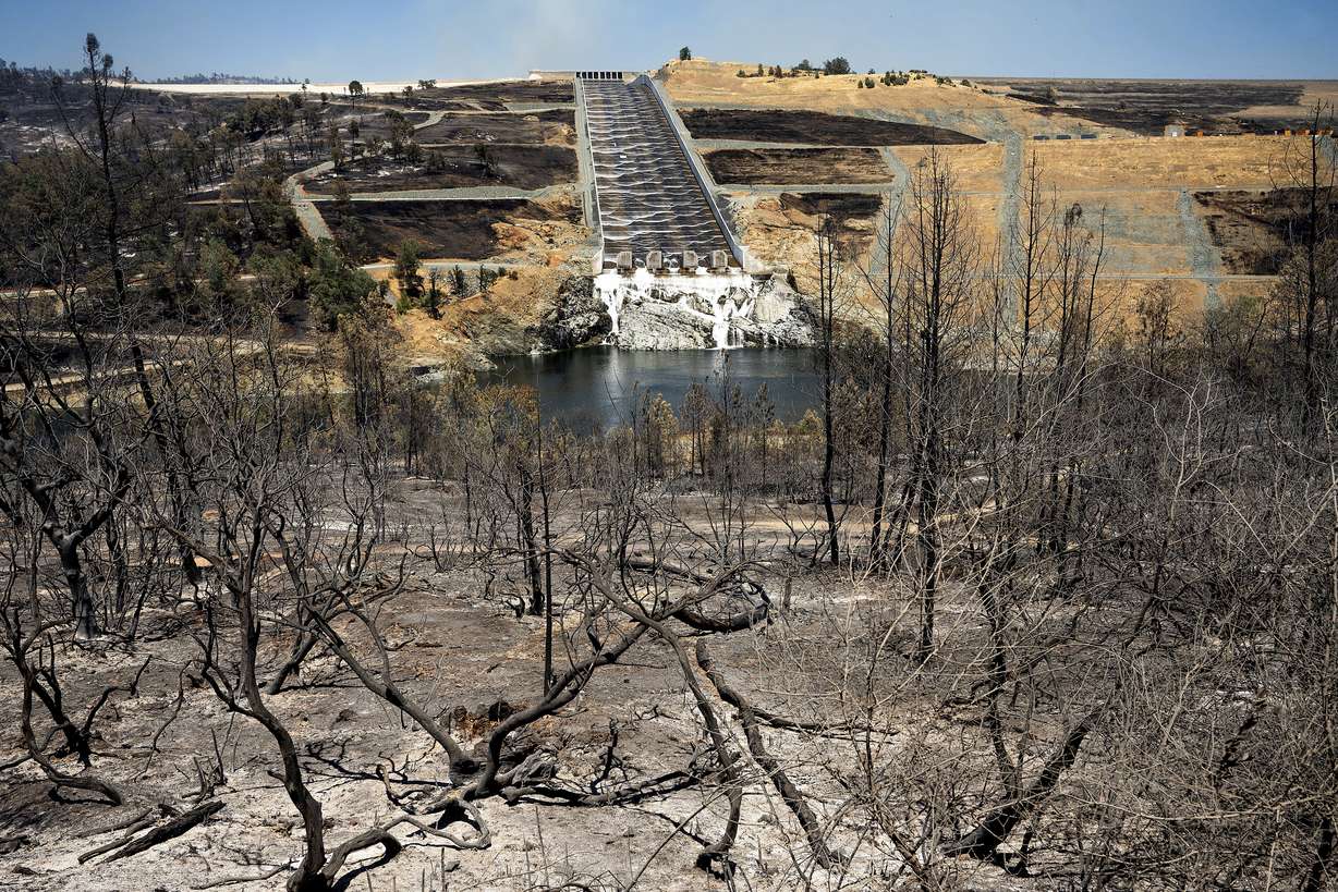 Water flows down the Oroville Dam spillway behind vegetation scorched in the Thompson Fire, in Oroville, Calif., Wednesday. An extended heatwave blanketing Northern California has resulted in red flag fire warnings and power shutoffs.