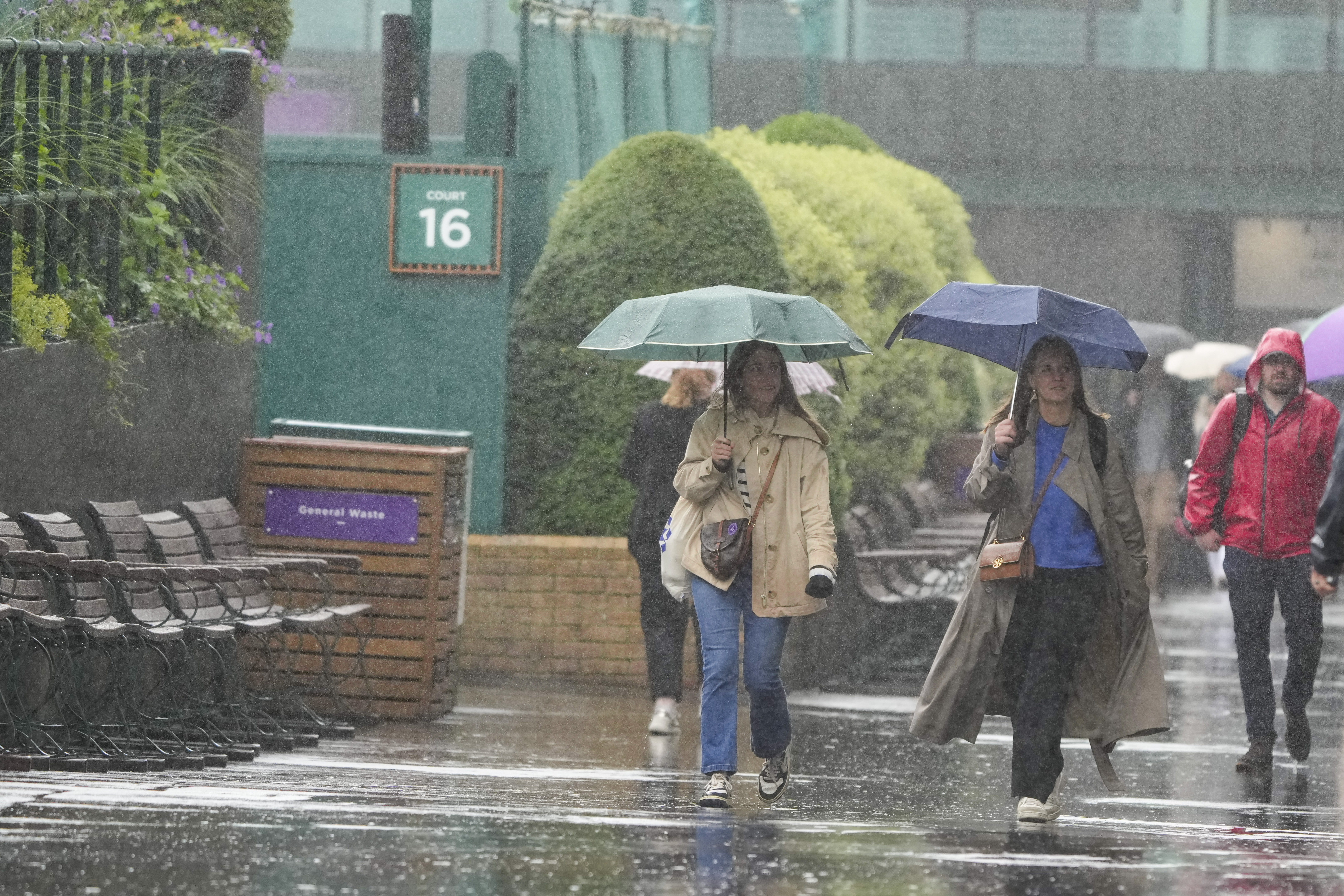 Spectators walk around the venue as rain delays the start of play ahead of third round matches at the Wimbledon tennis championships in London, Friday, July 5, 2024.