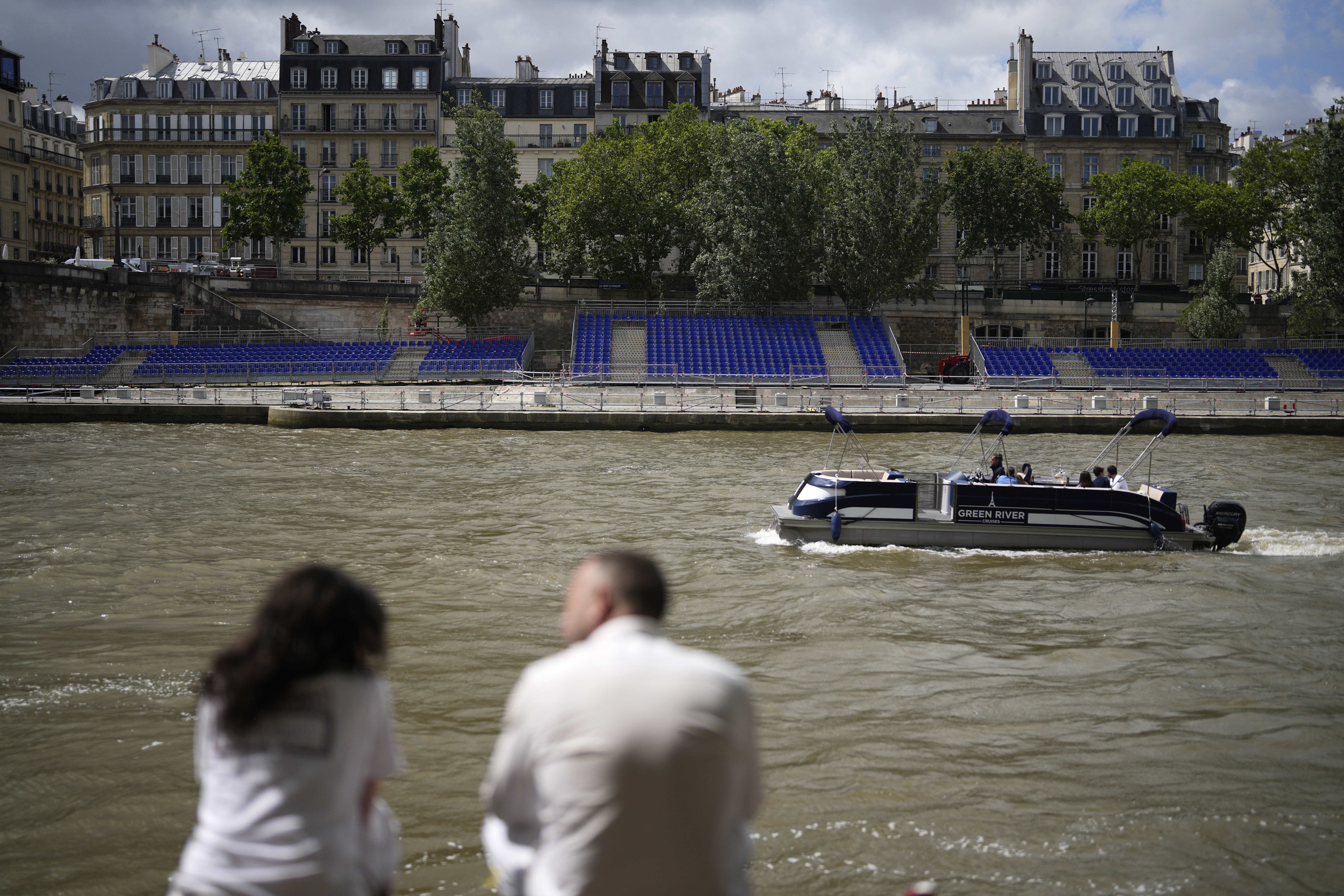 People sit along the Seine river with stands installed on its banks, Thursday, July 4, 2024 in Paris. The Seine river will host the Paris Olympic Games opening ceremony on July 26.