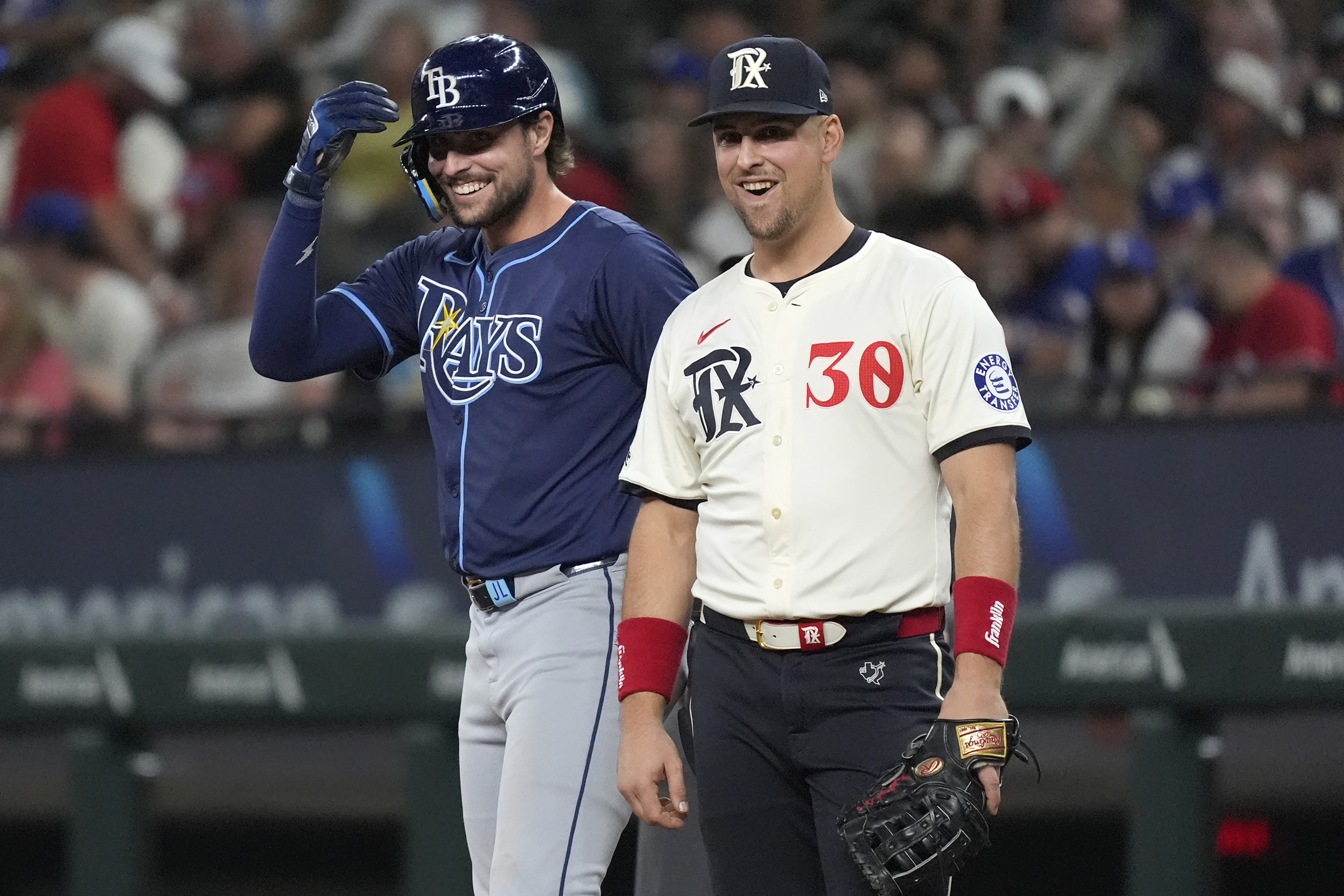 Texas Rangers first baseman Nathaniel Lowe (30) and his brother Tampa Bay Rays' Josh Lowe, left, laugh at first base after Josh singled during the sixth inning of a baseball game in Arlington, Texas, Friday, July 5, 2024. 