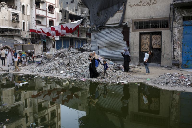 Palestinians displaced by the Israeli air and ground offensive on the Gaza Strip walk next a dark streak of sewage flowing into the streets of the southern town of Khan Younis, Gaza Strip, Thursday.