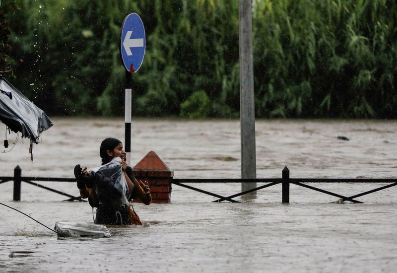 A woman carrying her belongings wades through a flooded road along the bank of overflowing Bagmati River following heavy rains in Kathmandu, Nepal, Saturday.