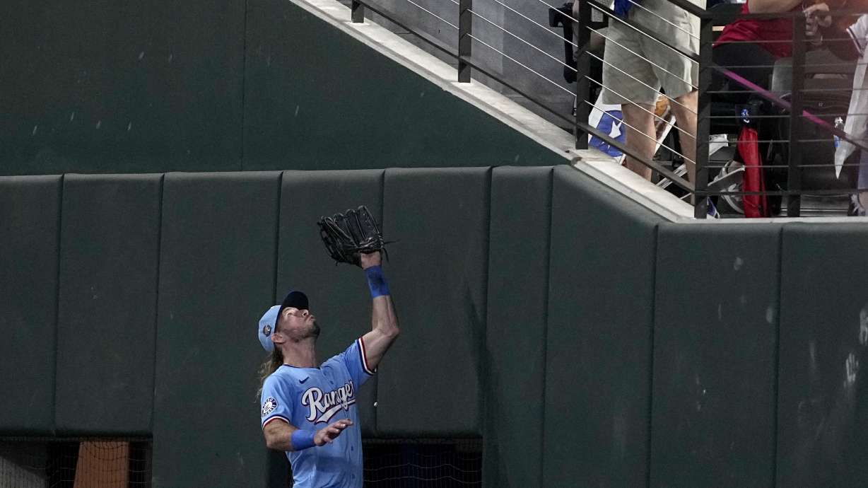 Texas Rangers right fielder Travis Jankowski, bottom, tries to catch a fly ball hit by Tampa Bay Rays' Randy Arozarena that a fan, top, catches in the seventh inning of a baseball game in Arlington, Texas, Sunday, July 7, 2024. Arozarena was called out on fan interference.