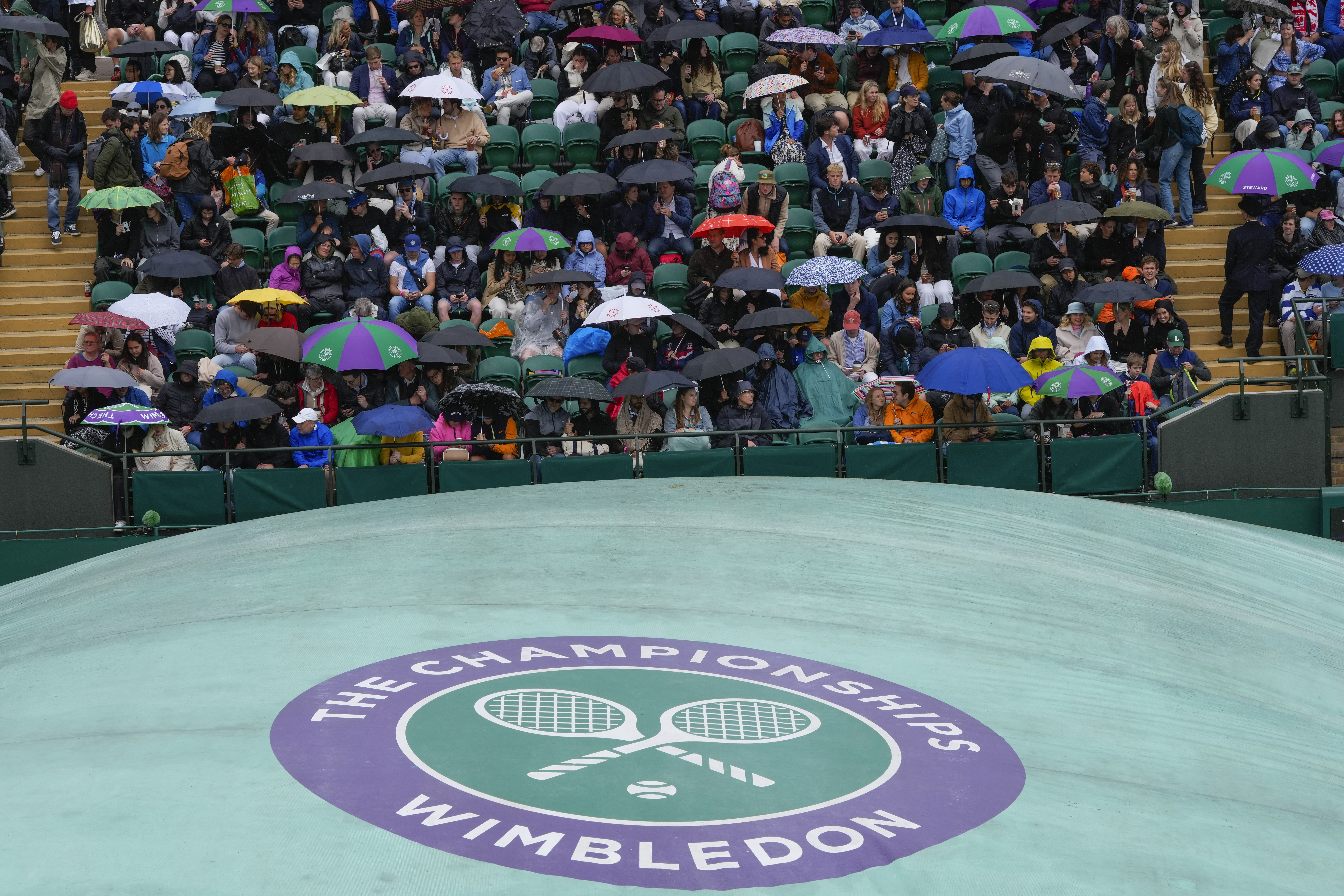 Spectators wait on an outside court as rain delays the start of play at the Wimbledon tennis championships in London, Saturday, July 6, 2024. 