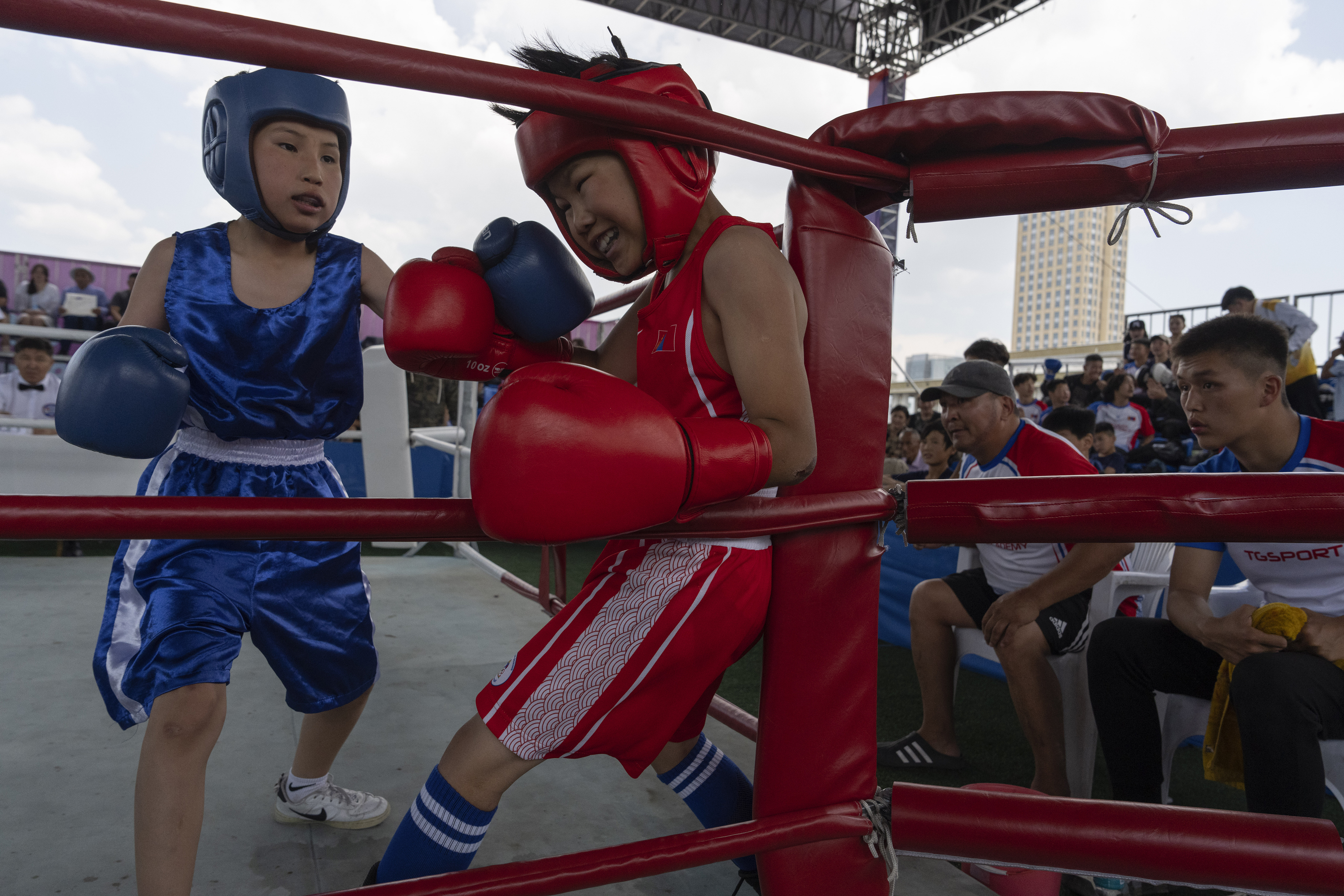 Twelve-year-old Gerelt-Od Kherlen, in red, defends against an attack from his opponent during a bronze medal boxing match on Sukhbaatar Square in Ulaanbaatar, Mongolia, Tuesday, July 2, 2024. Growing up in a Ger district without proper running water, Gerelt-Od fetched water from a nearby kiosk every day for his family. Carrying water and playing ball with his siblings and other children made him strong and resilient. 