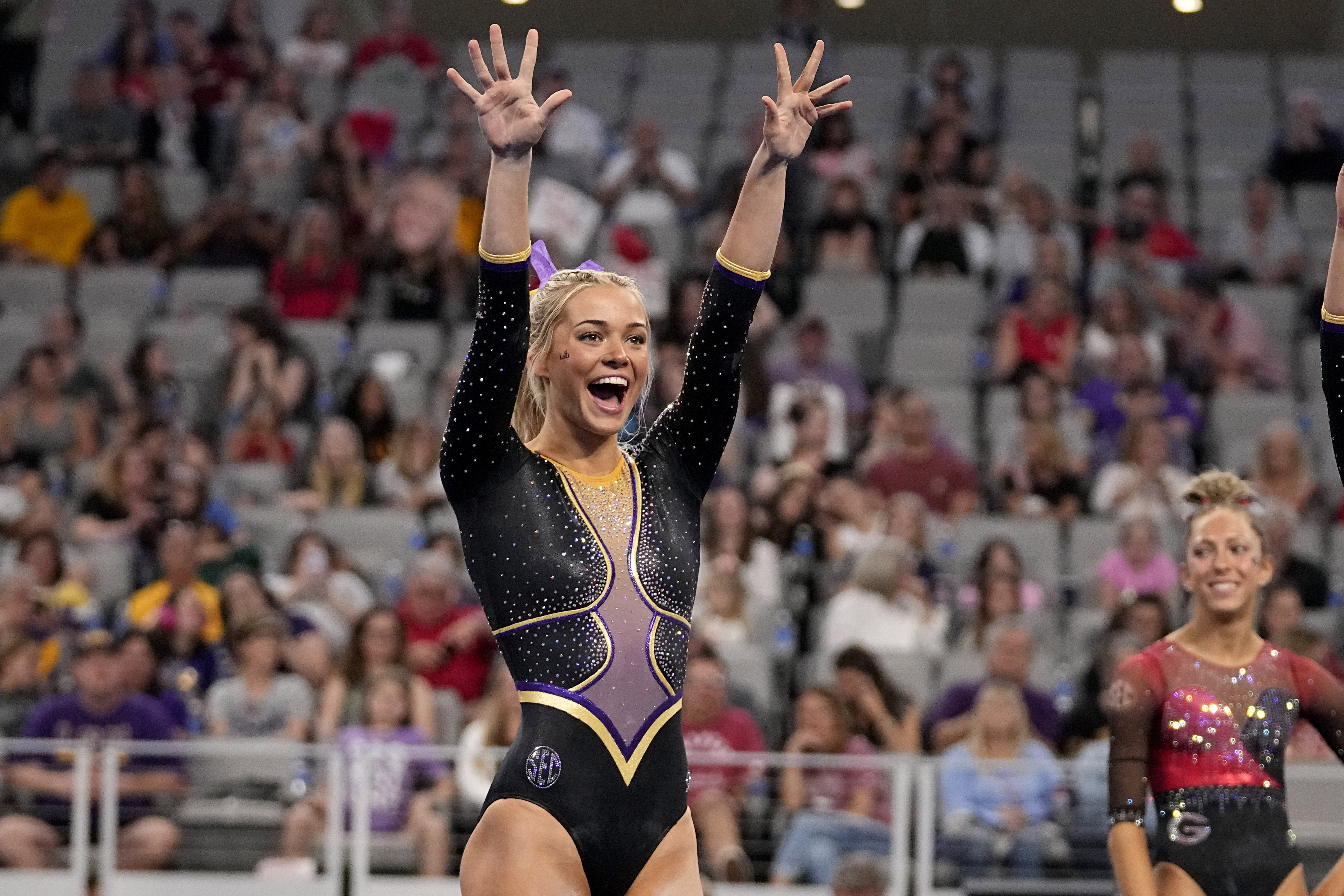 FILE - LSU's Olivia Dunne waves to fans cheering for the team as competitors warm up for the floor exercise during the NCAA women's gymnastics championships in Fort Worth, Texas, Thursday, April 18, 2024. Dunne will return for a fifth season at LSU, saying on social media she’s “not Dunne yet.” 