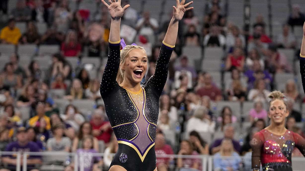 FILE - LSU's Olivia Dunne waves to fans cheering for the team as competitors warm up for the floor exercise during the NCAA women's gymnastics championships in Fort Worth, Texas, Thursday, April 18, 2024. Dunne will return for a fifth season at LSU, saying on social media she’s “not Dunne yet.”