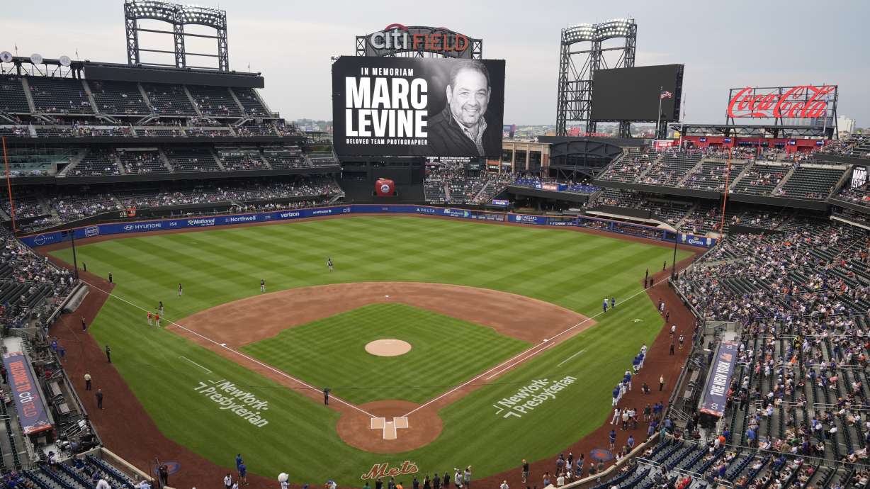 Fans and players stand during a moment of silence for New York Mets Chief Photographer Marc Levine before a baseball game between the New York Mets and the Washington Nationals, Tuesday, July 9, 2024, in New York. Levine passed away on Thursday, July 4.