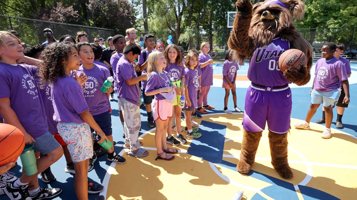 YouthCity kids watch as Jazz Bear gets ready to shoot the ball backwards over his head during a ribbon-cutting ceremony for a renovated community basketball court on Thursday.