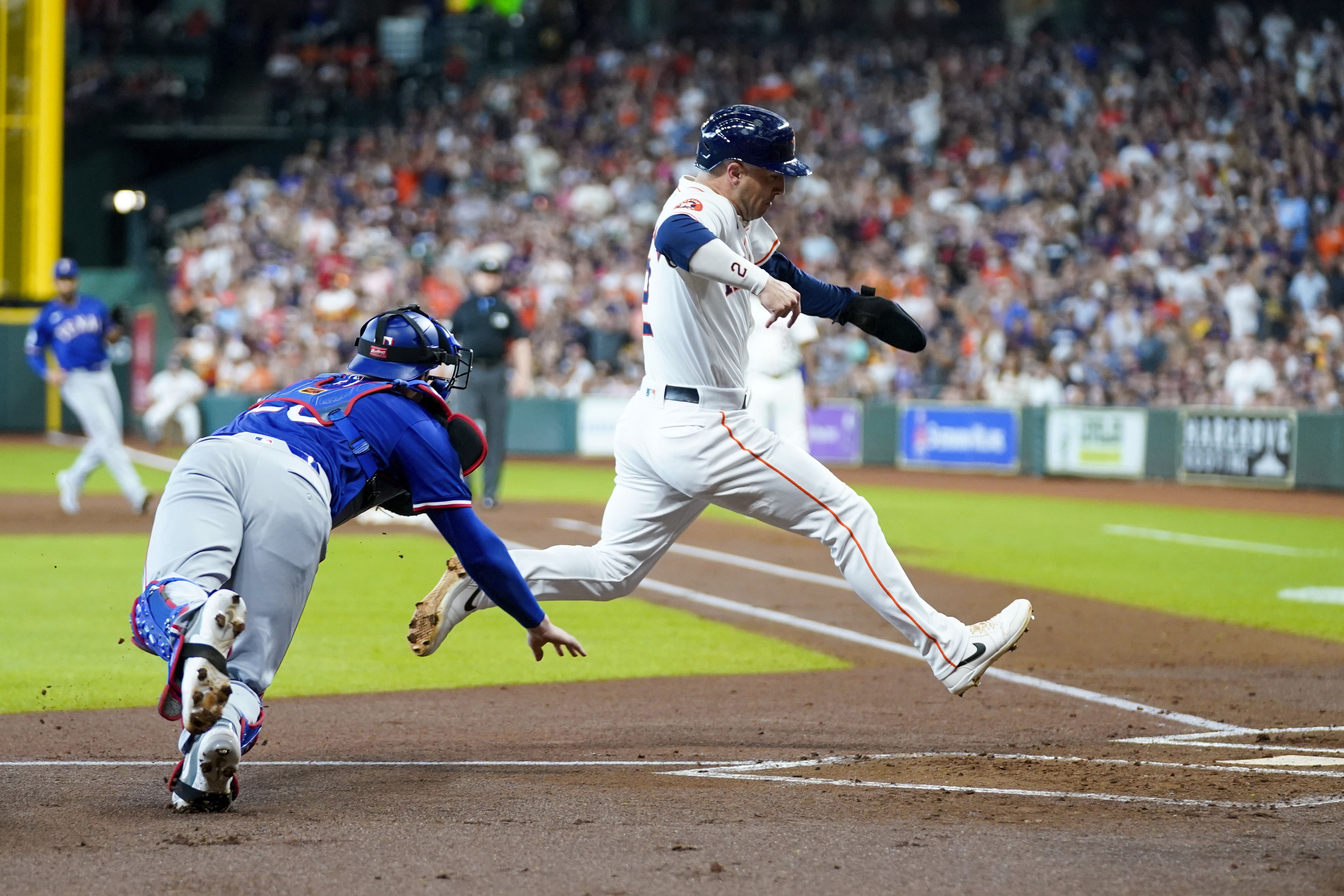 Houston Astros' Alex Bregman, right, avoids a tag by Texas Rangers catcher Jonah Heim, left, to score in the first inning of a baseball game Saturday, July 13, 2024, in Houston. 