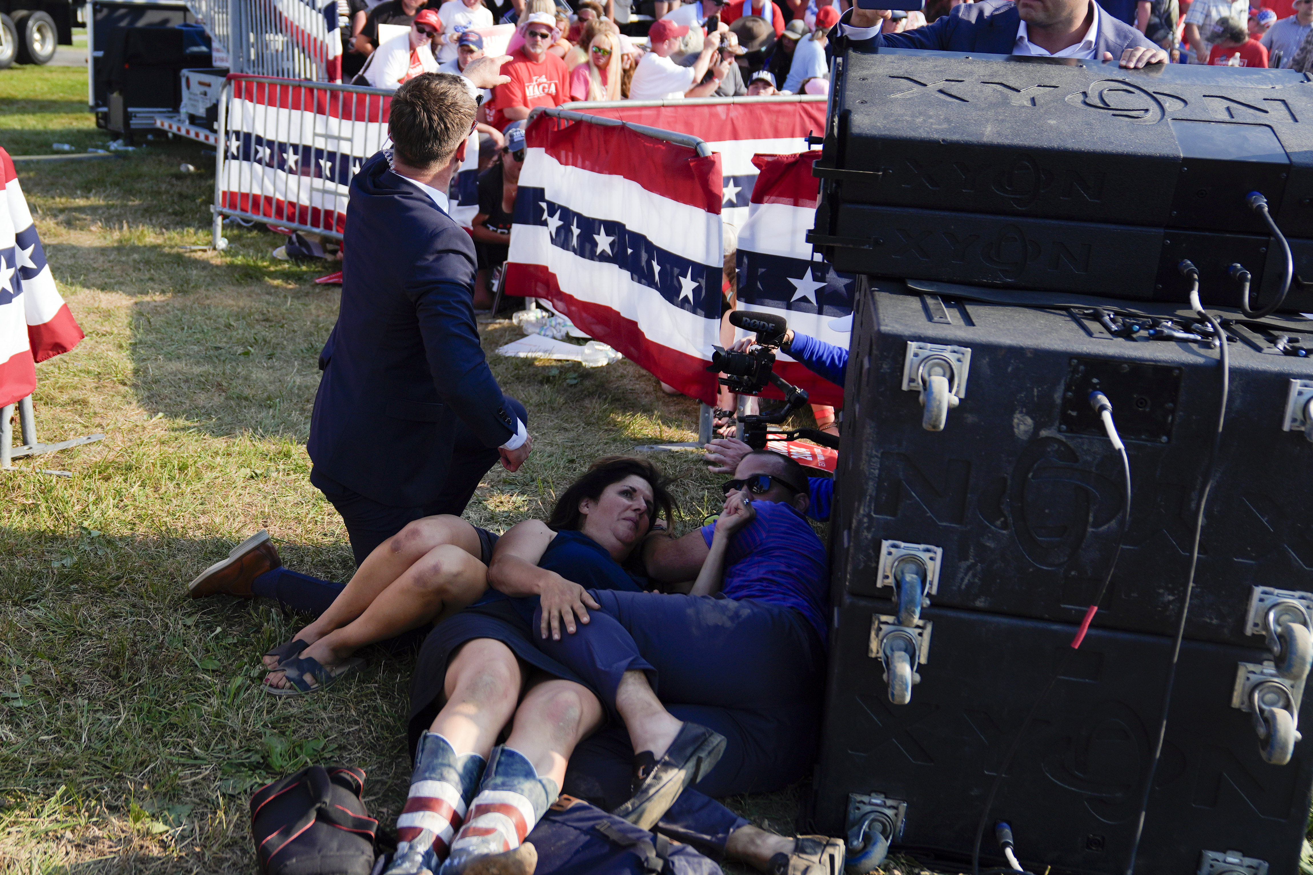 People take cover as U.S. Secret Service agents surround Republican presidential candidate former President Donald Trump on stage at a campaign rally, Saturday, in Butler, Pa.