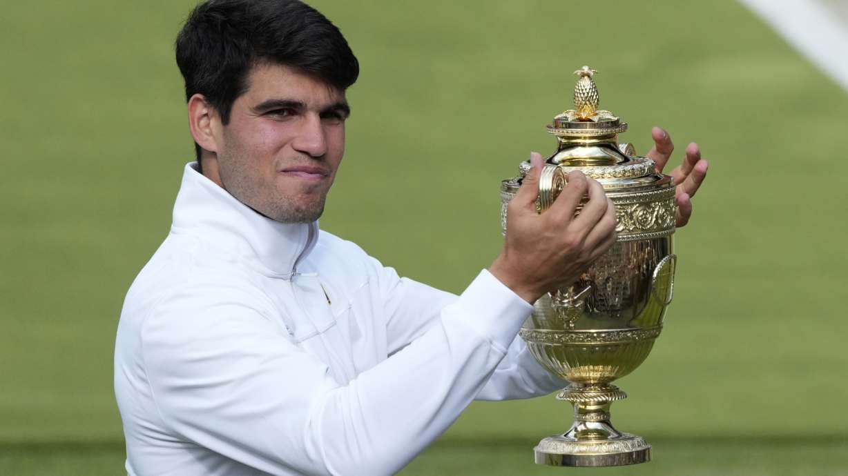 Carlos Alcaraz of Spain smiles as he holds up his trophy for the photographers after defeating Novak Djokovic of Serbia in the men's singles final at the Wimbledon tennis championships in London, Sunday, July 14, 2024.