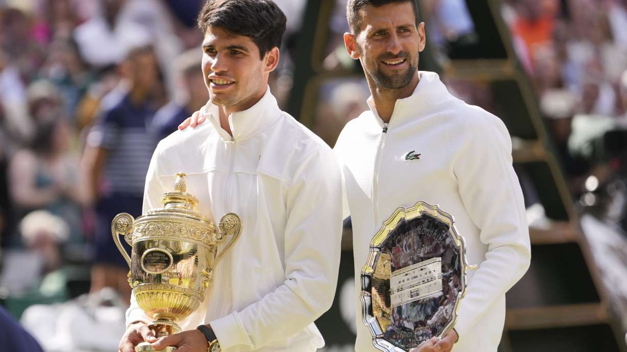 Carlos Alcaraz of Spain holds his trophy as he stands with Novak Djokovic of Serbia after winning the men's singles final at the Wimbledon tennis championships in London, Sunday, July 14, 2024.