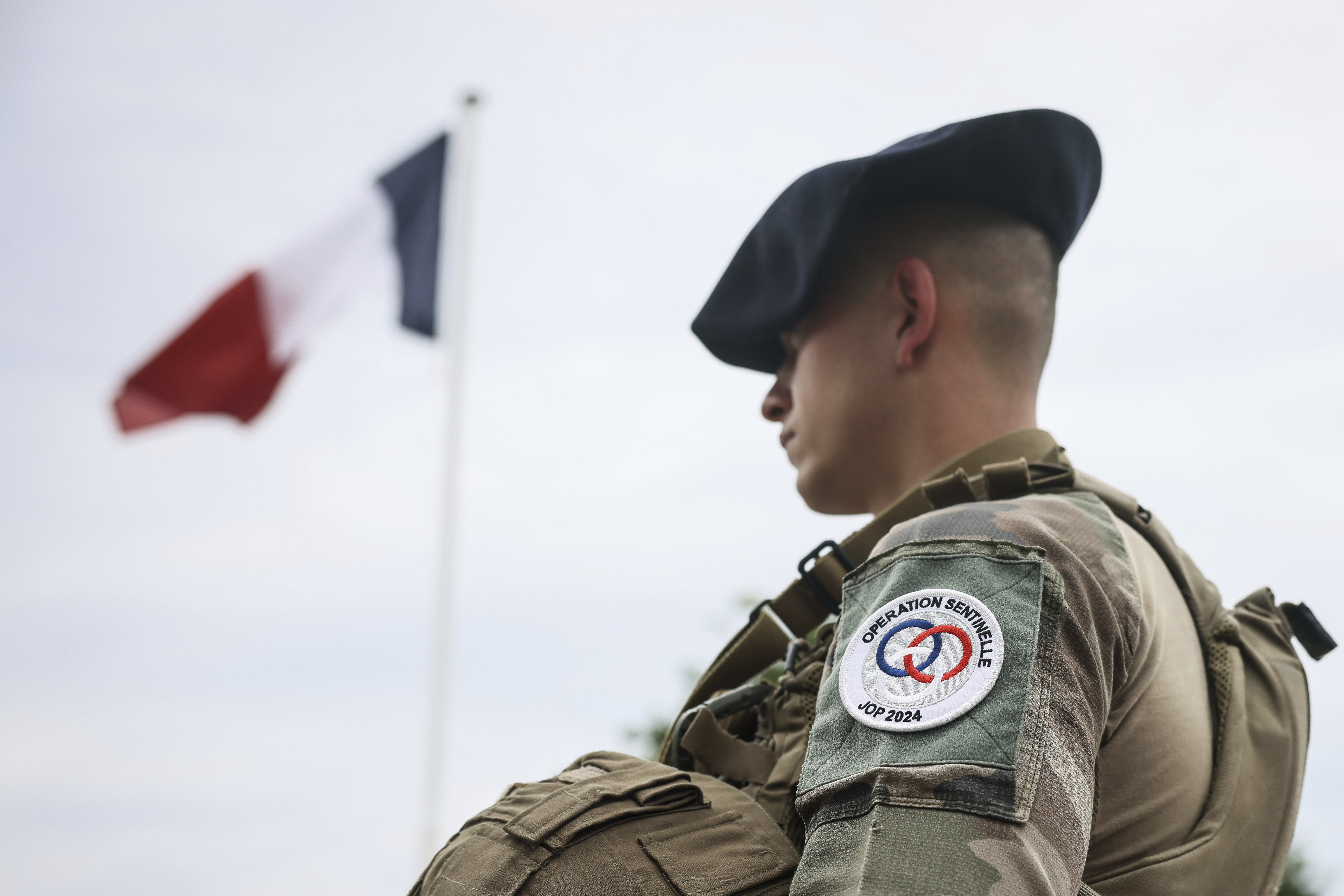 A soldier stands by the French flag at the military camp set up in the Vincennes woods, Monday, July 15, 2024 just outside Paris. The military camp, with prefabricated barracks and sleeping stretchers, is being built in the east of Paris to house 4,500 soldiers assigned to security during the Paris 2024 Olympic Games. 