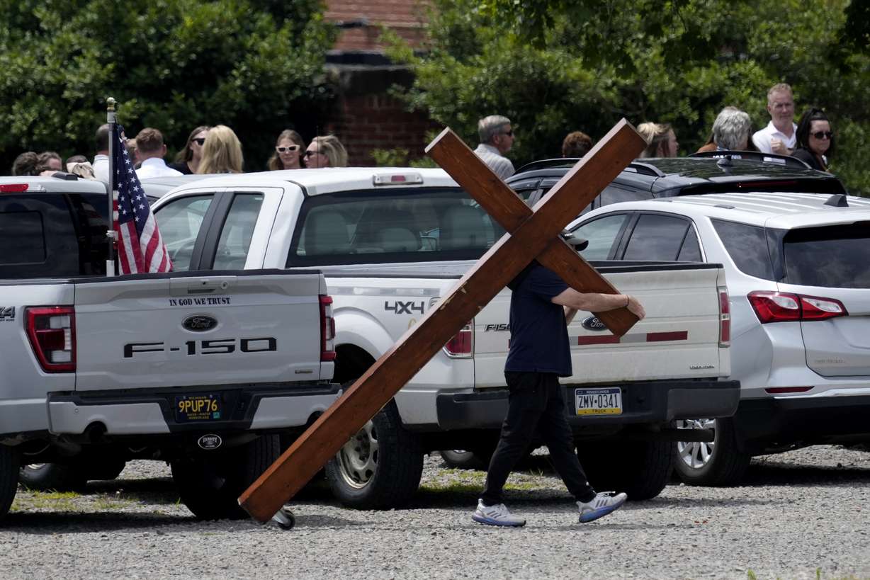 Dan Beazley carries a cross past a line of guests at a visitation for Corey Comperatore at Laube Hall, Thursday, in Freeport, Pennsylvania. Comperatore was killed at rally for former President Donald Trump Saturday.