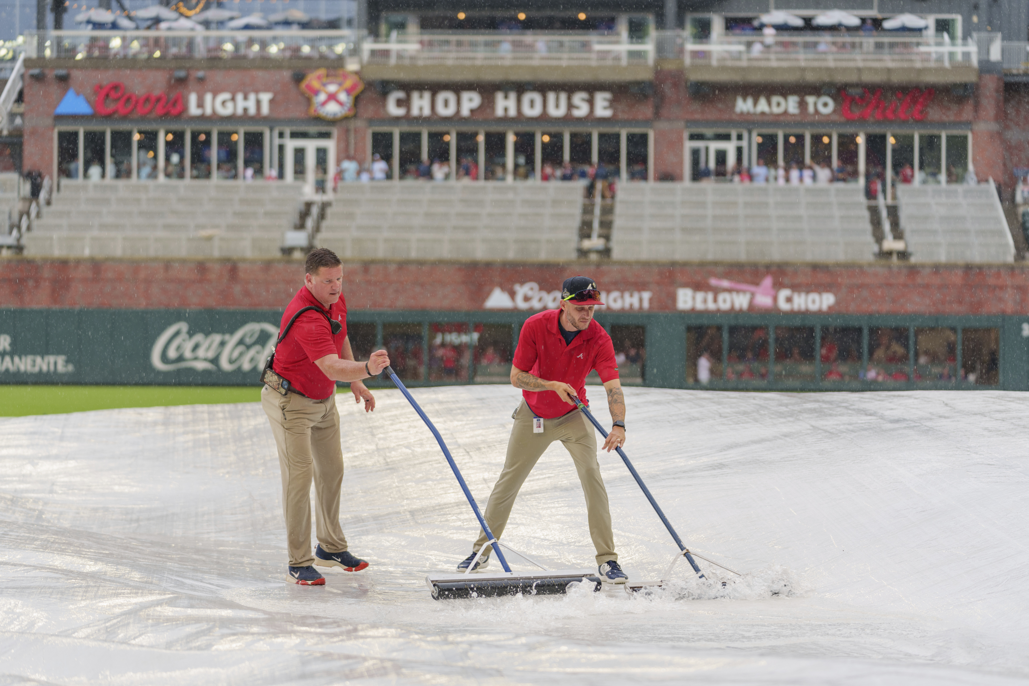 Field staff push rainwater off of a tarp over the infield during the rain delay of a baseball game between the Atlanta Braves and the St. Louis Cardinals, Friday, July 19, 2024, in Atlanta. 