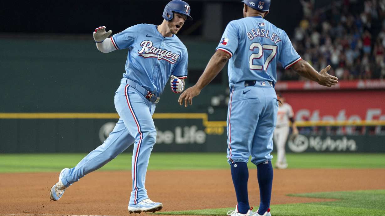 Texas Rangers' Jonah Heim, left, is congratulated by third base coach Tony Beasley (27) as he rounds third on his three-run home run that also scored Wyatt Langford and Nathaniel Lowe during the fourth inning of a baseball game against the Baltimore Orioles, Sunday, July 21, 2024, in Arlington, Texas.