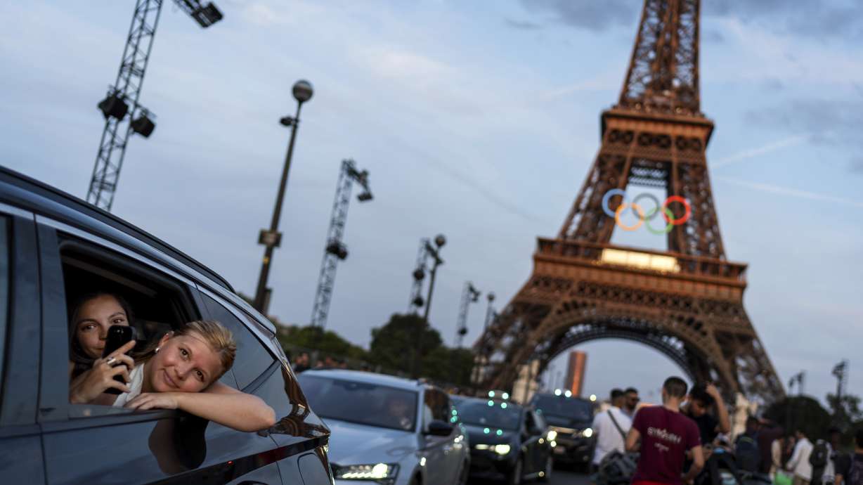FILE - Passengers in the back of a taxi film themselves as they leave the Eiffel Tower decorated with the Olympic rings ahead of the 2024 Summer Olympics, Wednesday, July 17, 2024, in Paris. The city itself will be one of the protagonists of the 2024 Olympics. That's why the Eiffel Tower and Seine River are featured just as prominently as Simone Biles or Katie Ledecky in NBC’s ads.