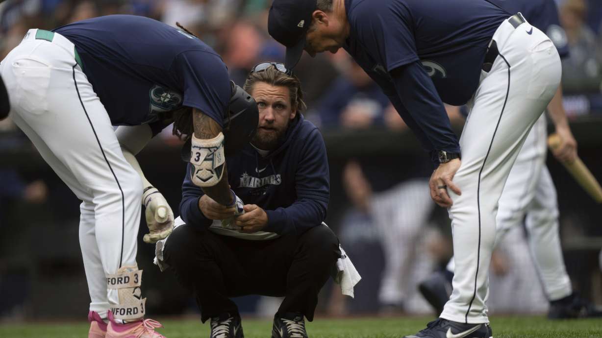 Seattle Mariners' J.P. Crawford, left, is checked by a team trainer, center, and manager Scott Servais, right, after getting hit by a pitch during the first inning of a baseball game against the Los Angeles Angels, Monday, July 22, 2024, in Seattle.