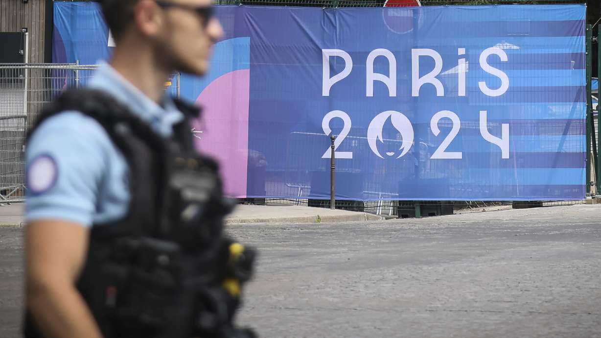 FILE - A police officer walks past a Paris Olympics canvas at the 2024 Summer Olympics, Saturday, July 20, 2024, in Paris, France. Three days before the start of the Olympics, France's Interior Minister has hailed the country’s law enforcement for their hard work in making the Paris Games safe for 10,500 athletes and millions of visitors.