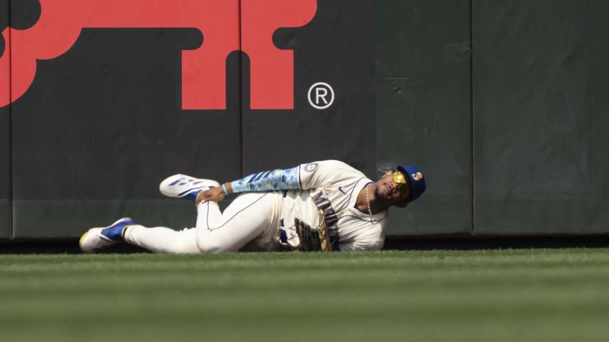 Seattle Mariners centerfielder Julio Rodriguez hold his leg after crashing into the outfield wall while trying to catch the ball during the sixth inning of a baseball game against the Houston Astros, Sunday, July 21, 2024, in Seattle.