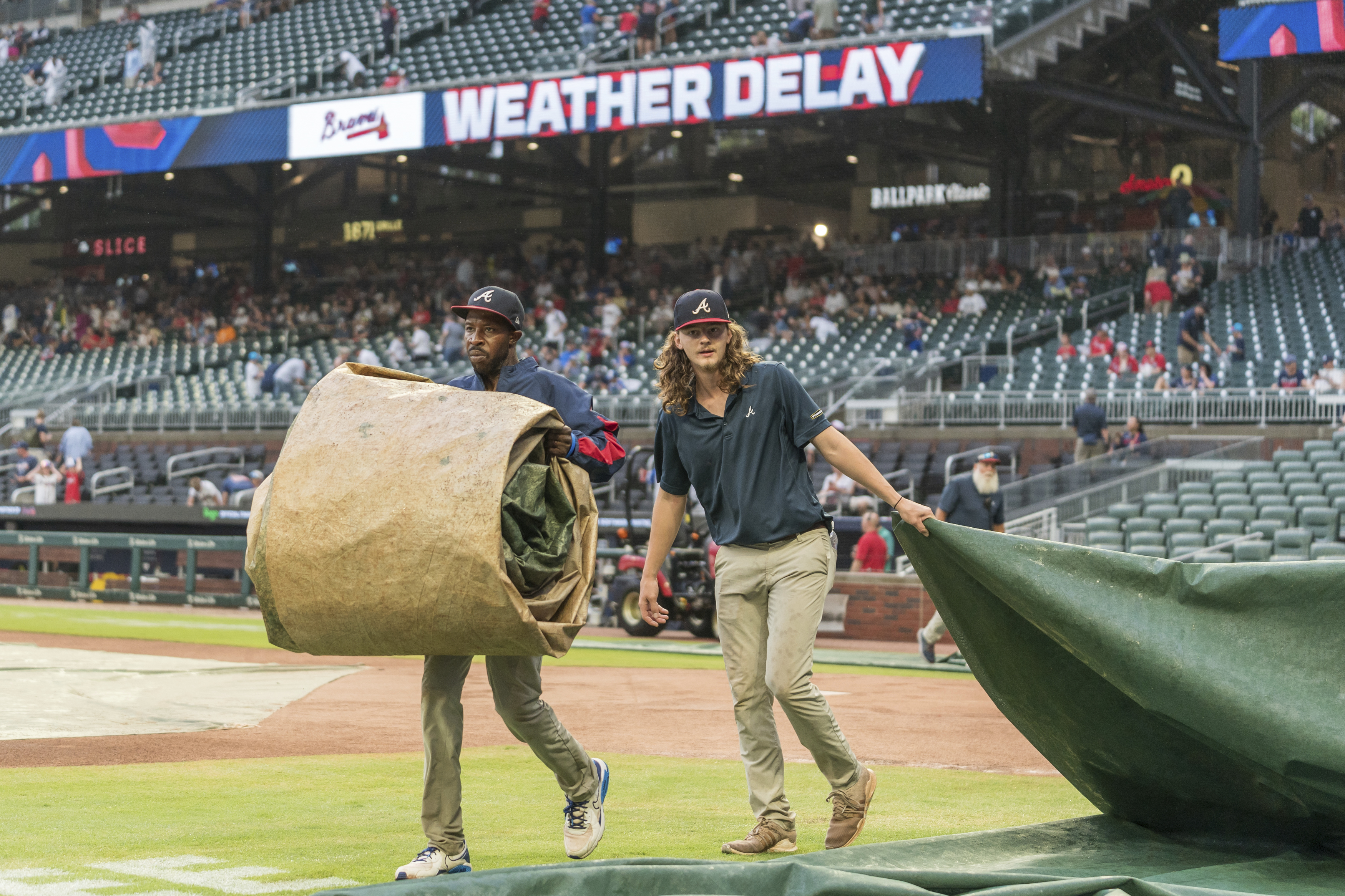 Ground crew workers remove tarps before a baseball game between the Cincinnati Reds and Atlanta Braves, Tuesday, July 23, 2024, in Atlanta. 