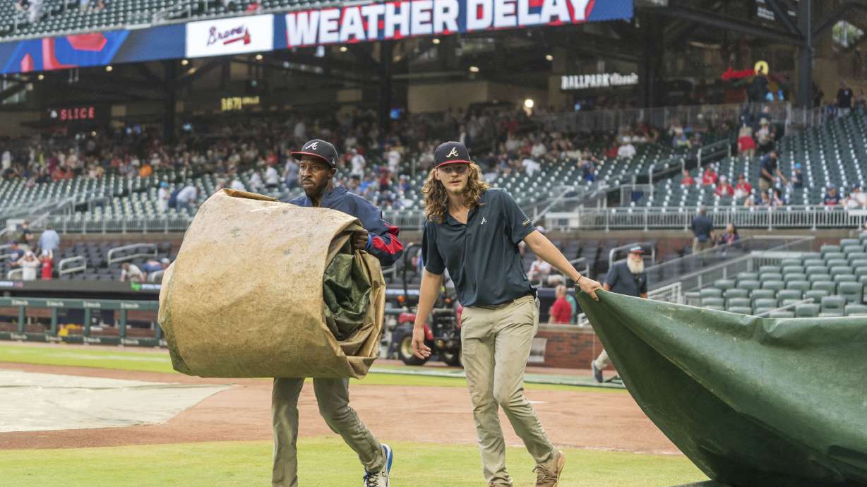 Ground crew workers remove tarps before a baseball game between the Cincinnati Reds and Atlanta Braves, Tuesday, July 23, 2024, in Atlanta.