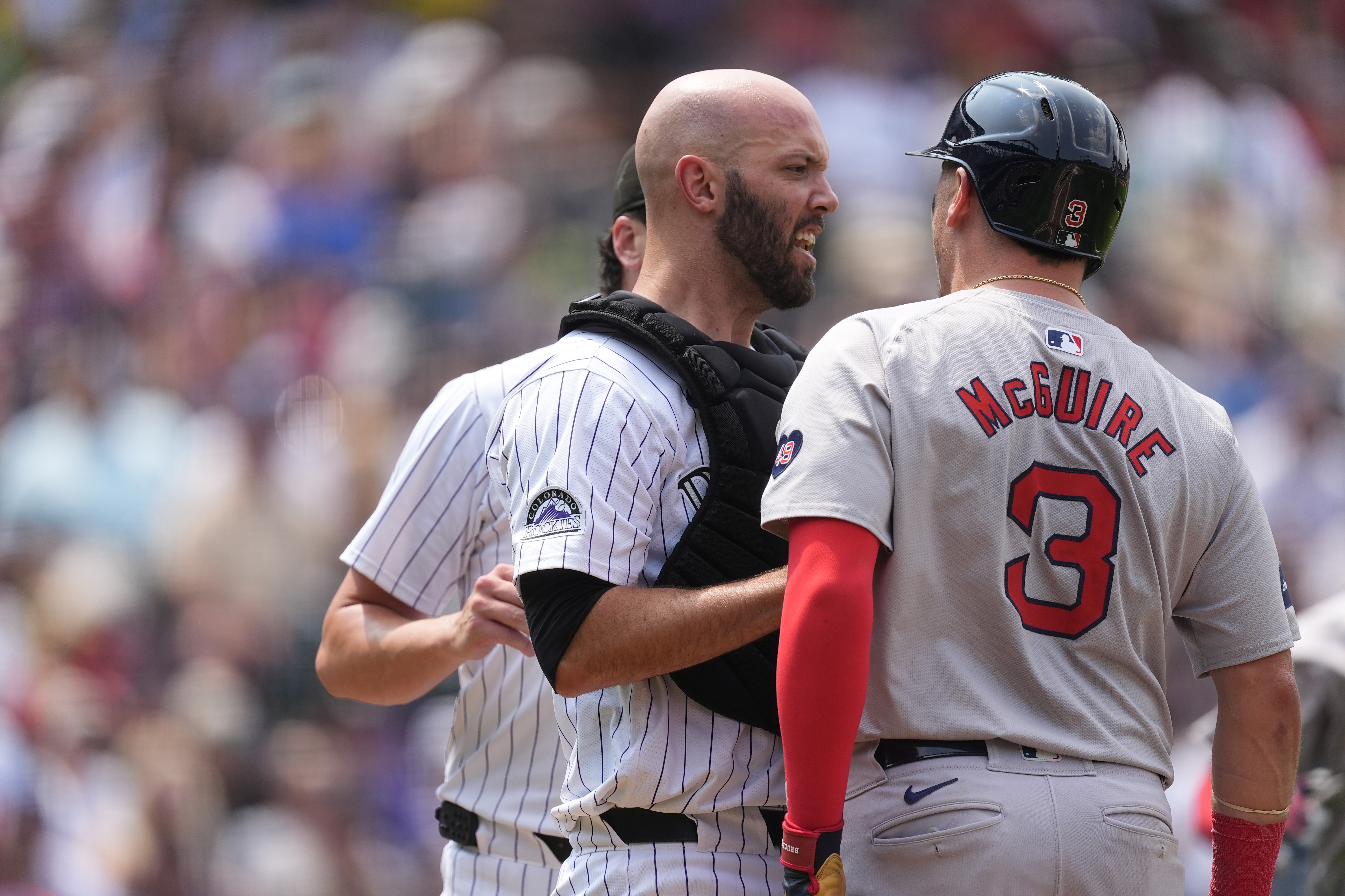 Colorado Rockies catcher Jacob Stallings, front left, stands in between starting pitcher Cal Quantrill, back let, and Boston Red Sox's Reese McGuire as they argue after McGuire flied out to end the top of the fourth inning of a baseball game Wednesday, July 24, 2024, in Denver. 