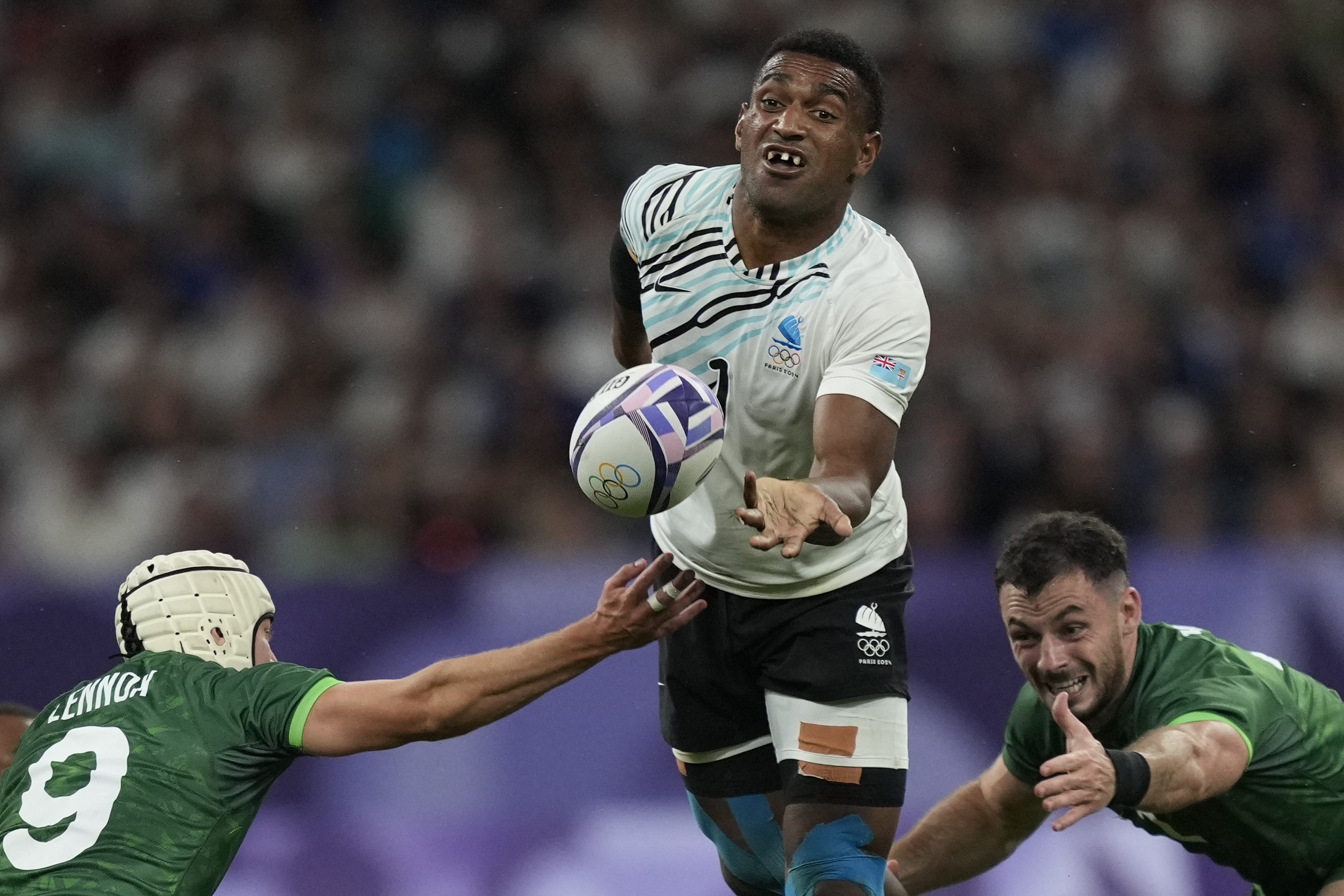 Fiji's Joji Nasova passes the ball as Ireland's Hugo Lennox, left tackles during the men's quarterfinal match Rugby Sevens between Fiji and Ireland at the 2024 Summer Olympics, in the Stade de France, Thursday, July 25, 2024, in Saint-Denis, France. 