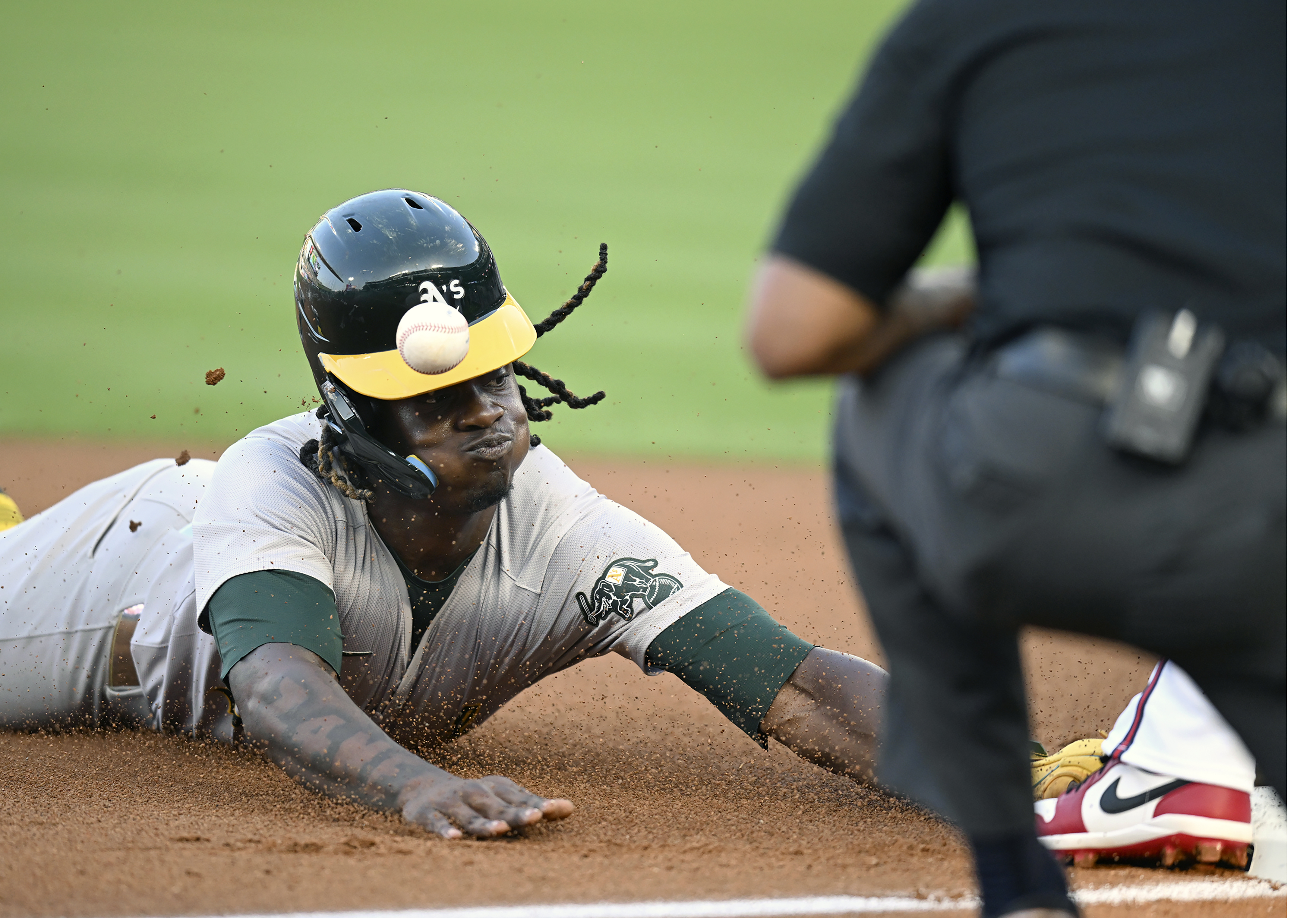 Oakland Athletics' Lawrence Butler, left, is hit on the helmet at third base during the first inning of a baseball game against the Los Angeles Angels, Thursday, July 25, 2024, in Anaheim, Calif. 