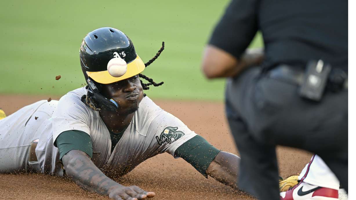 Oakland Athletics' Lawrence Butler, left, is hit on the helmet at third base during the first inning of a baseball game against the Los Angeles Angels, Thursday, July 25, 2024, in Anaheim, Calif.