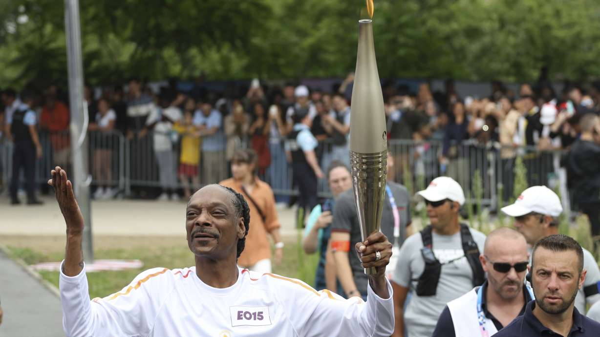 Snoop Dogg carries the Olympic torch at the 2024 Summer Olympics, Friday, July 26, 2024, in Saint-Denis, outside Paris, France.