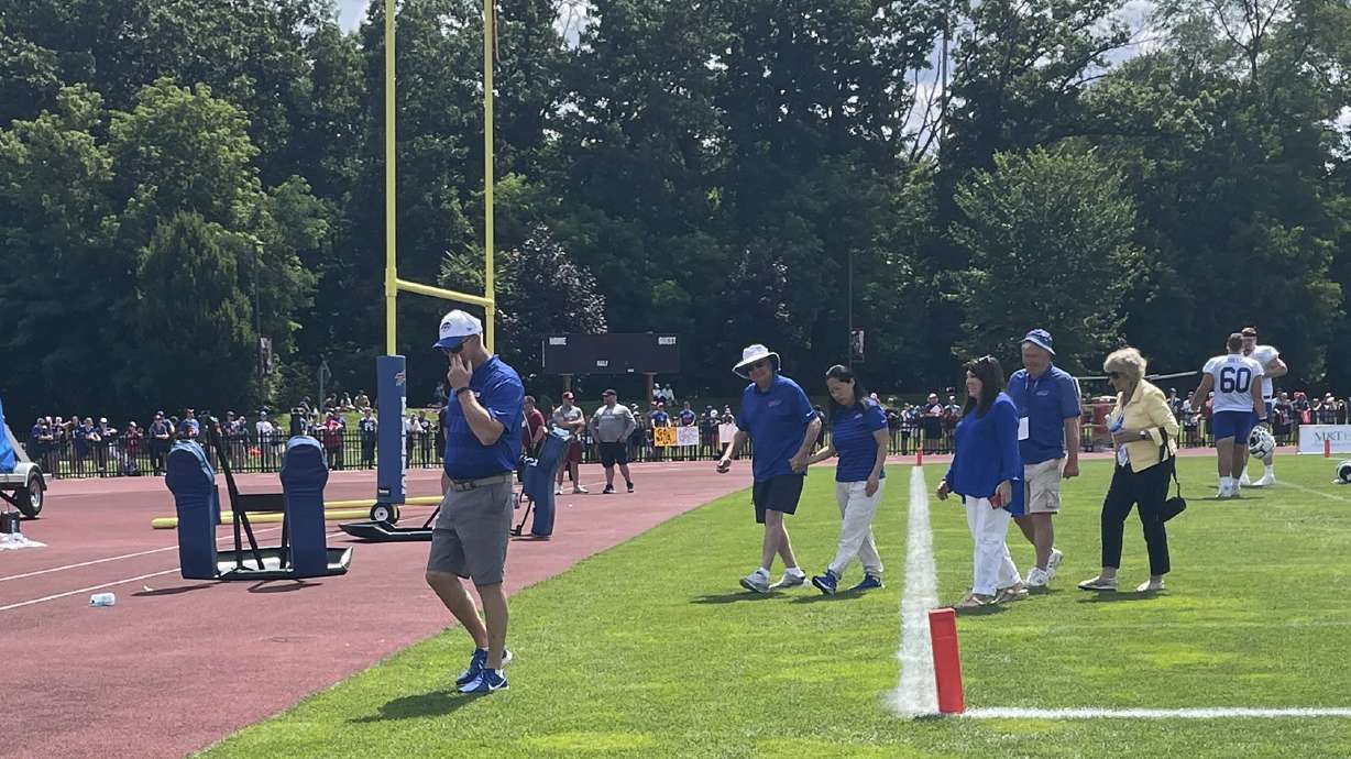 Buffalo Bills owner Terry Pegula holds his wife Kim Pegula's hand as he escorts her off the field after she met with the players in the end zone following the end of training camp in Pittsford, N.Y., Friday, July 26, 2024.
