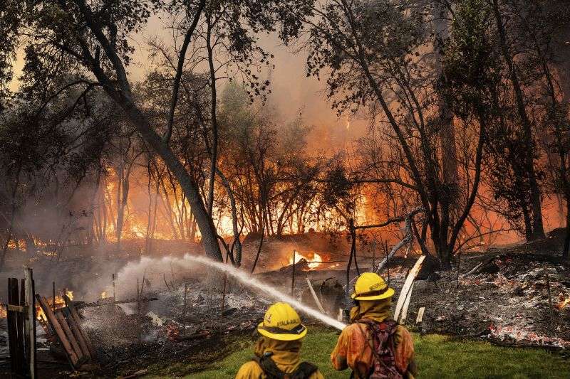 Firefighters spray water while battling the Park Fire in the Cohasset community of Butte County, Calif., on Thursday. The crew was able to keep flames from reaching the mobile home they were protecting.
