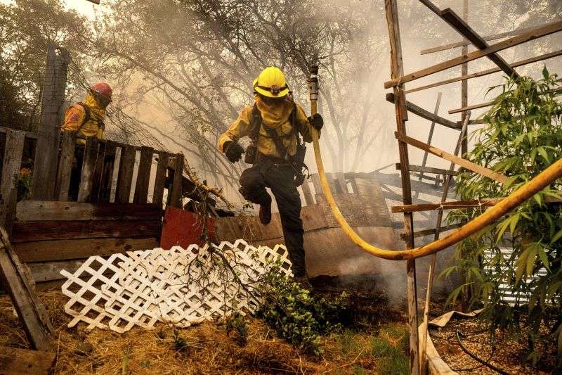Firefighter Christian Moorhouse jumps over a fence while battling the Park Fire in the Cohasset community of Butte County, Calif., on Thursday. His crew was able to keep flames from reaching the mobile home they were protecting.