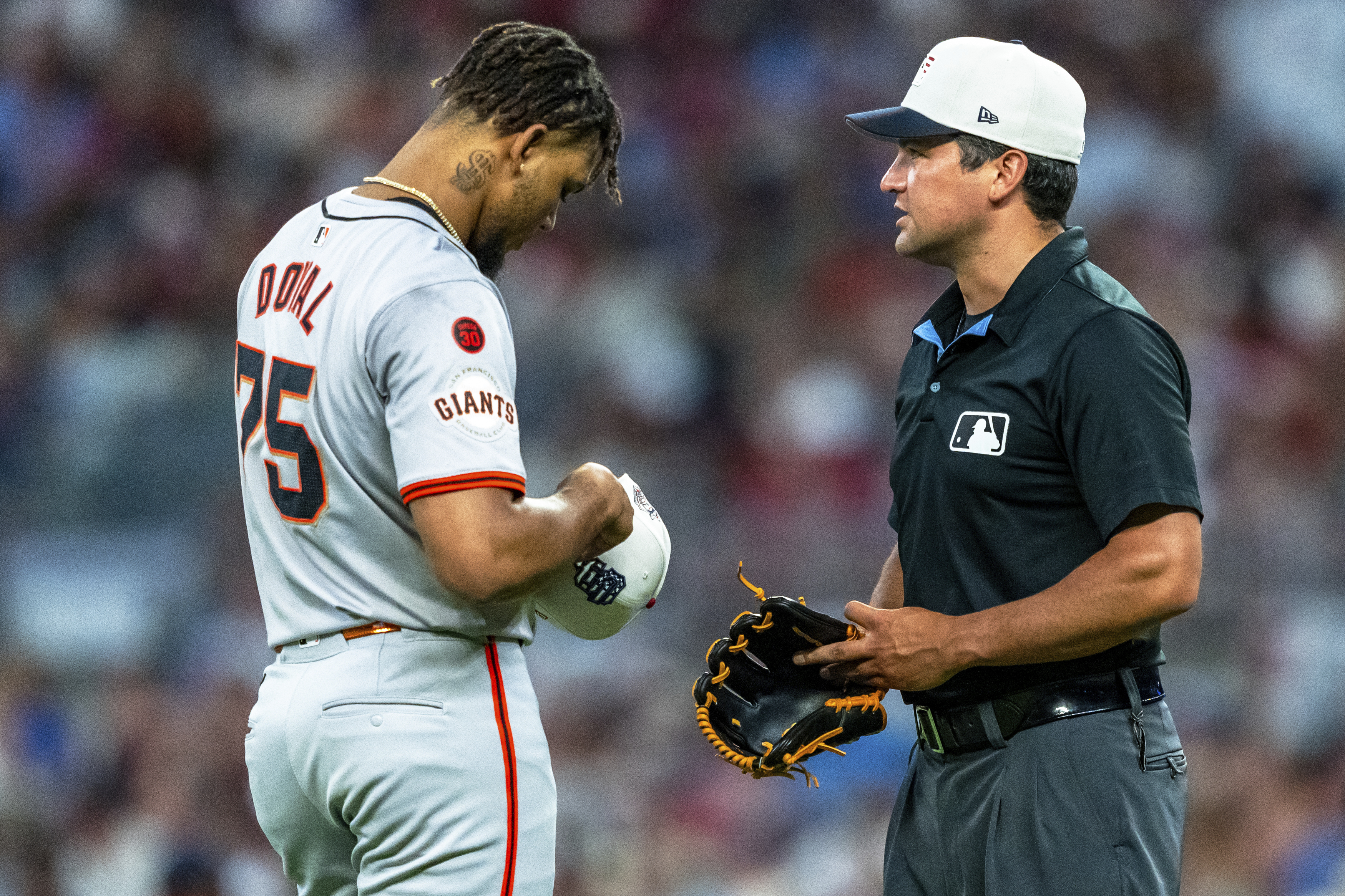 San Francisco Giants pitcher Camilo Doval (75) has his cap and glove checked by umpire Tony Randazzo, right, during the ninth inning of a baseball game against the Atlanta Braves, Thursday, July 4, 2024, in Atlanta. 