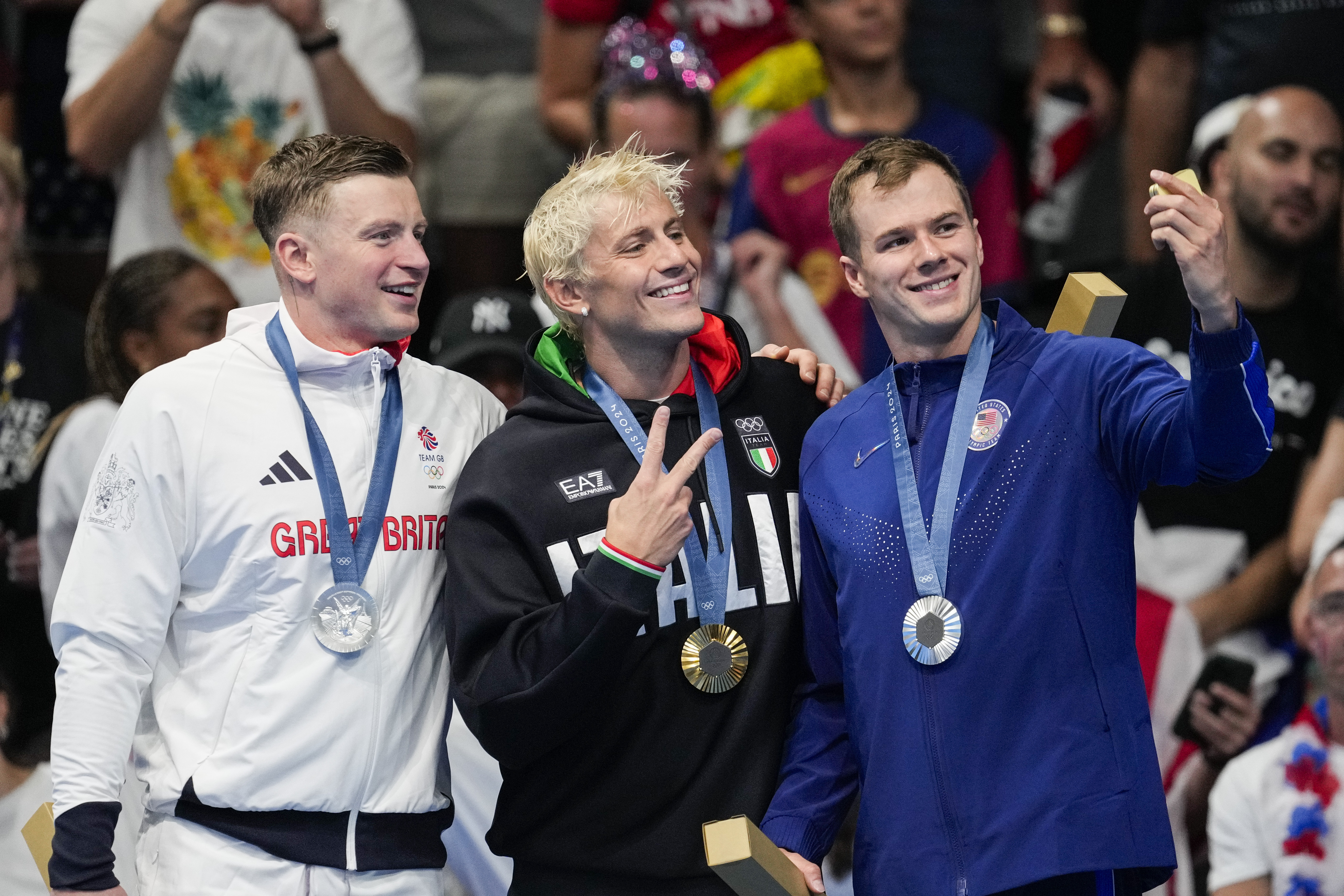 Gold medalist, Nicolo Martinenghi, center, of Italy, stands with silver medalists, Nic Fink, right, of the the United States, and Adam Peaty, of Britain, on the podium after the men's 100-meter breaststroke final at the 2024 Summer Olympics, Sunday, July 28, 2024, in Nanterre, France. 