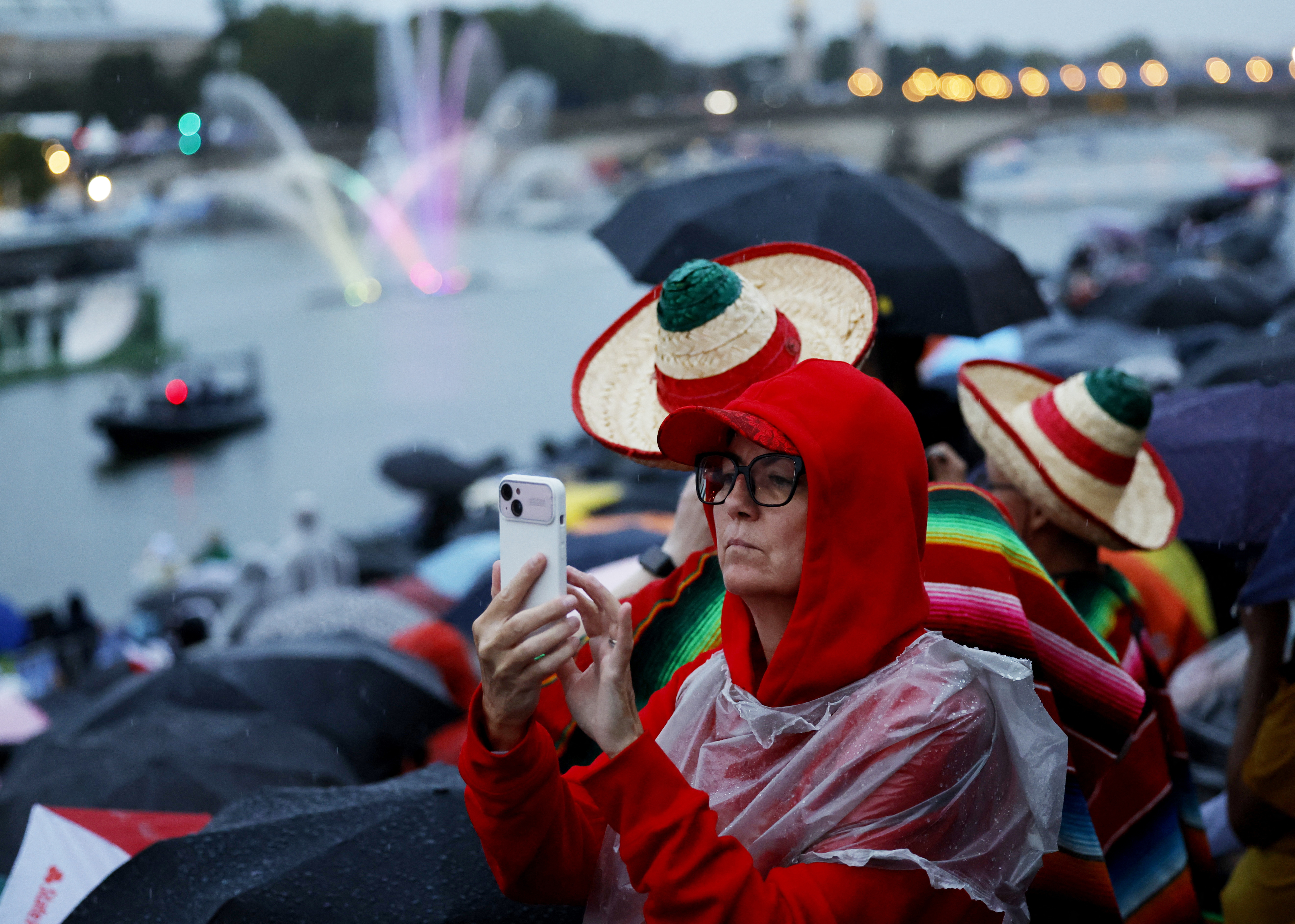 A spectator takes a photo on their phone as athletes ride in a boats along the Seine River during the opening ceremony for the 2024 Summer Olympics in Paris, France, Friday, July 26, 2024. 