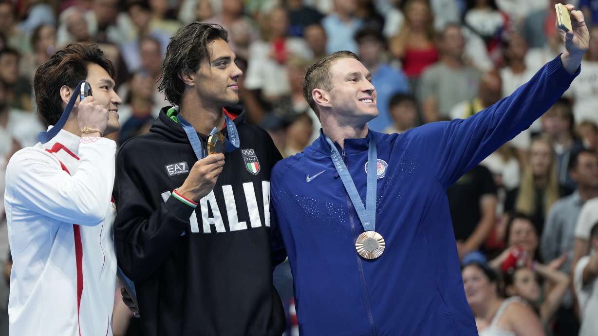 Gold medalist Thomas Ceccon, of Italy, stands on the podium with silver medalist Xu Jiayu, left, of China, and bronze medalist Ryan Murphy, right, of the United States, for a selfie following the men's 100-meter backstroke final at the 2024 Summer Olympics, Monday, July 29, 2024, in Nanterre, France.