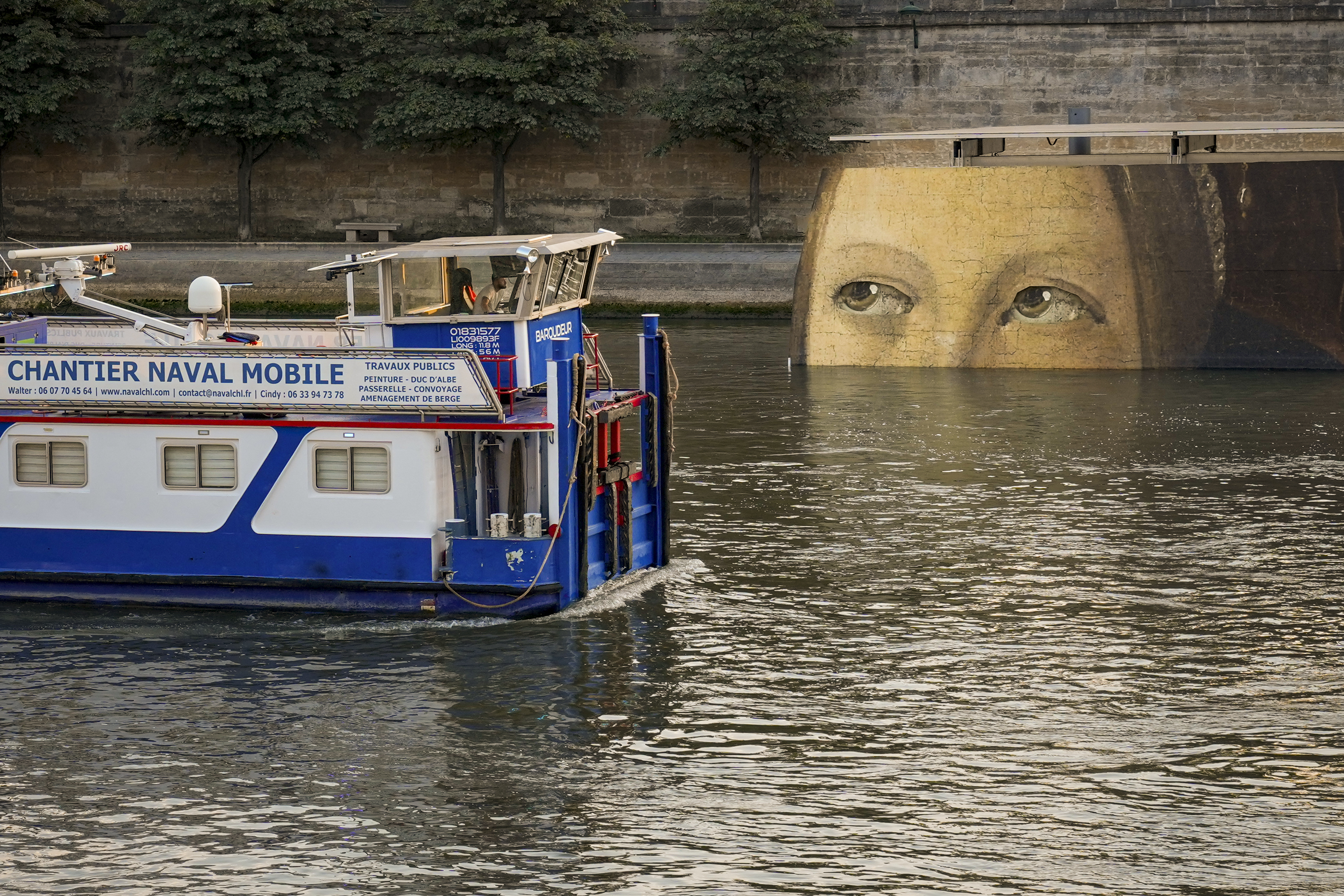 A ship sails past reproductions of artworks decorating the banks of the River Seineat the 2024 Summer Olympics, Tuesday, July 30, 2024, in Paris, France. The men's Olympic triathlon has been postponed over concerns about water quality in Paris' Seine River, where the swimming portion of the race was supposed to take place. 